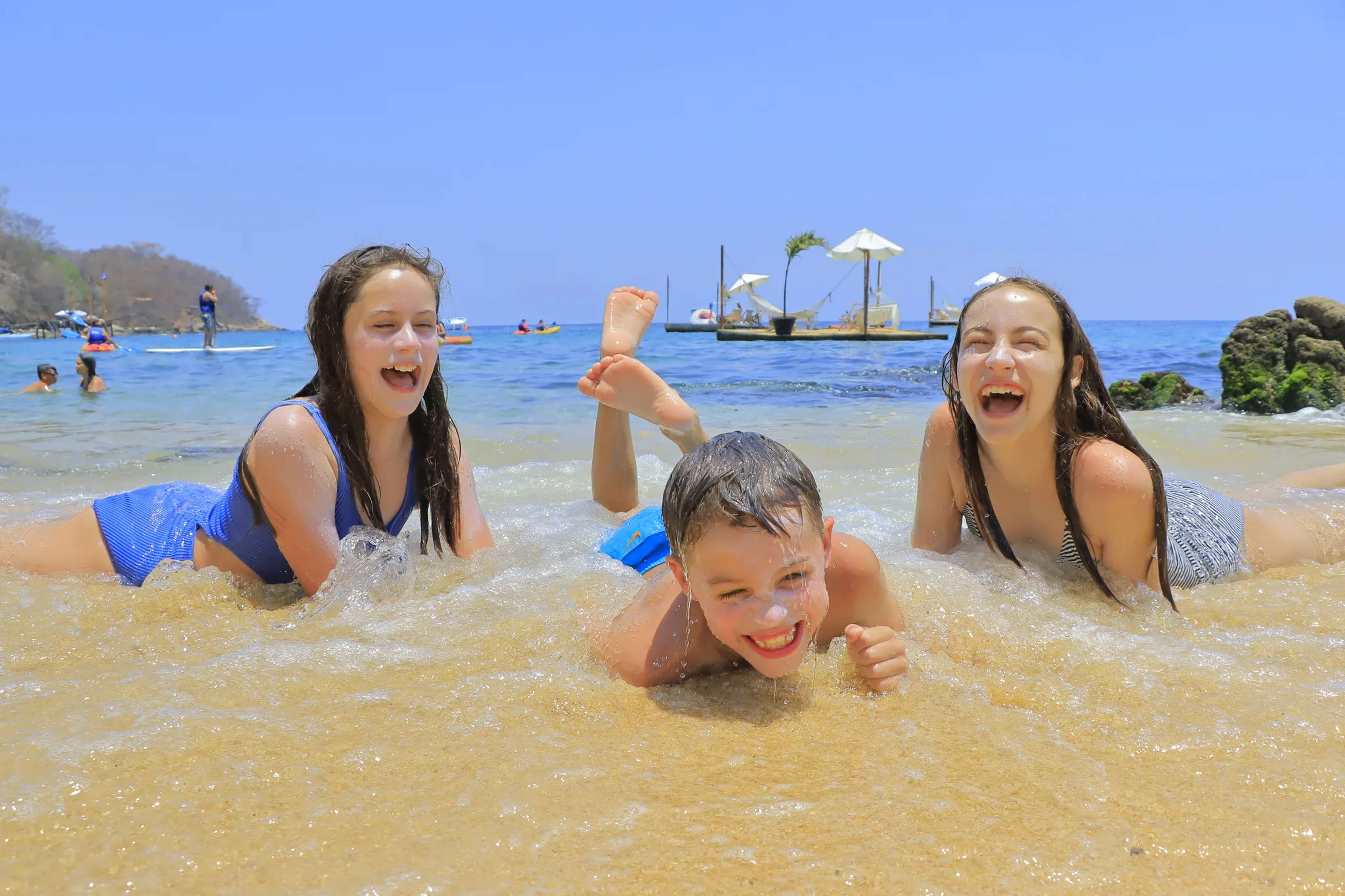Una familia juega en las aguas turquesas de la playa Las Caletas, con botes y otros visitantes visibles al fondo.