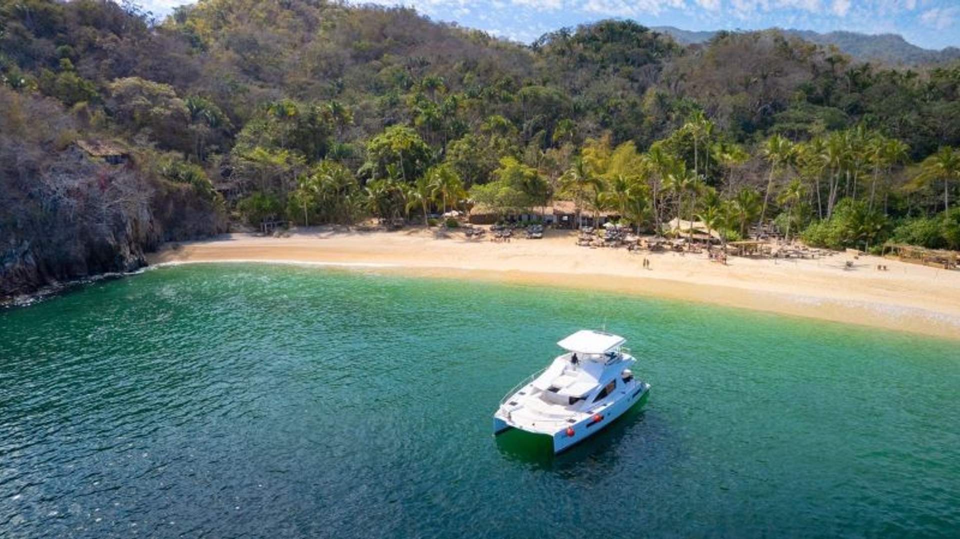 Yate anclado cerca de una playa tropical rodeada de un exuberante bosque.