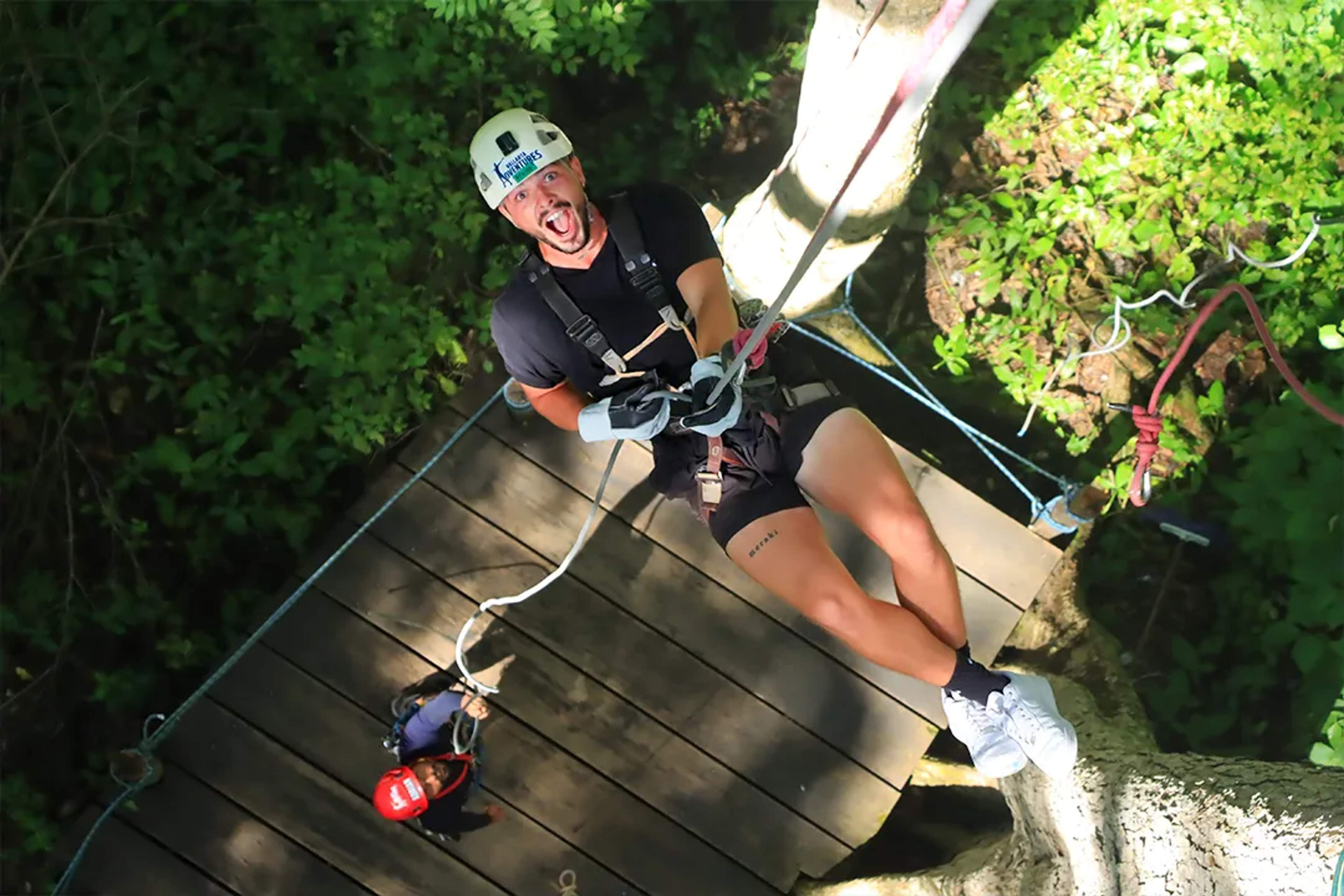 Excited adventurer rappelling down a tree platform in the middle of the jungle.