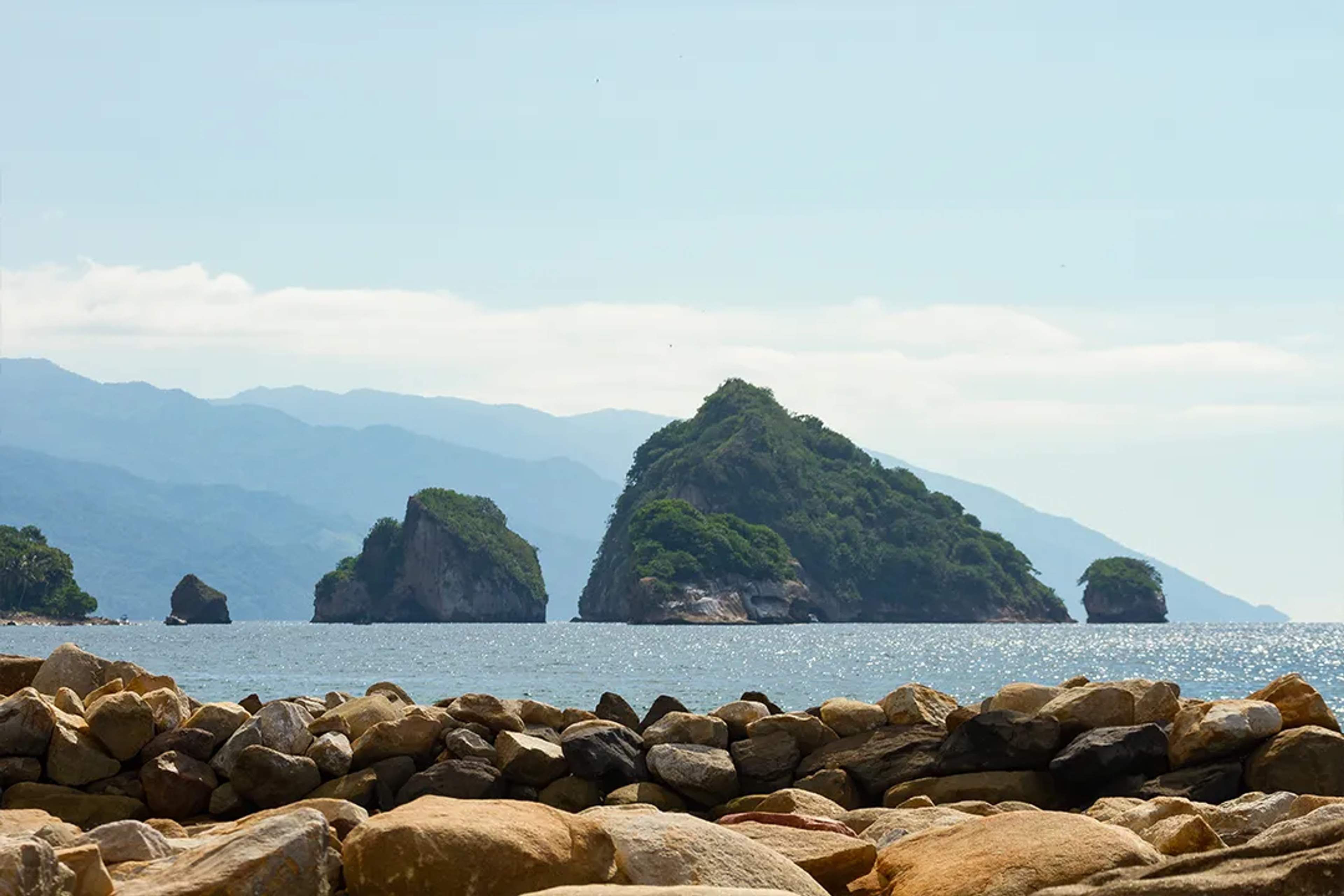 Los Arcos rock formations rise from the sea, framed by mountains and shoreline rocks in Vallarta.