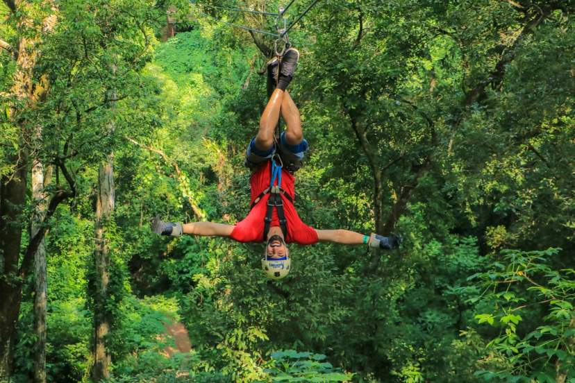 Adventurer ziplines upside down through lush jungle, arms wide open and full of excitement.