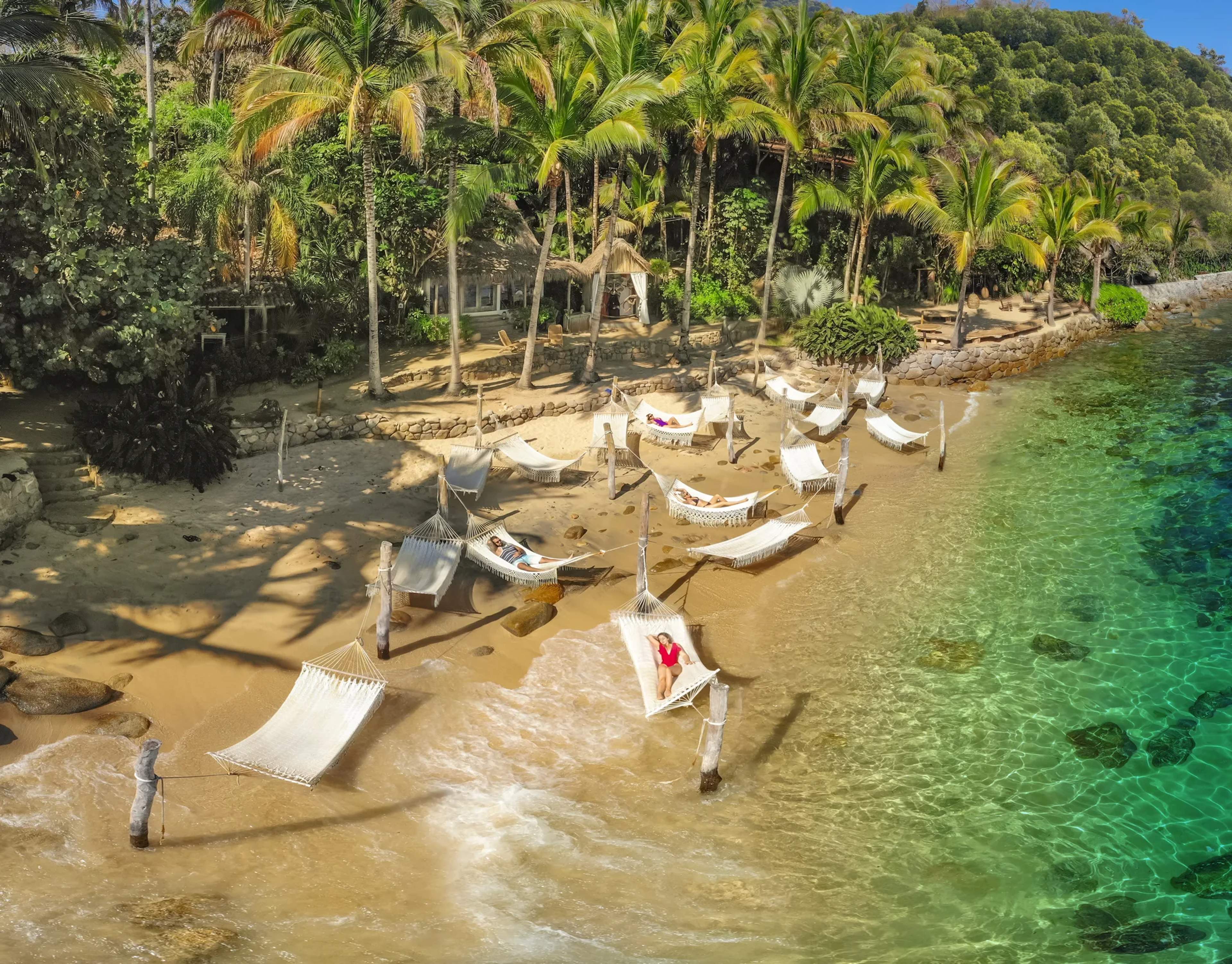 Moored boats, swaying palms, and crystal-clear turquoise water fill the secluded cove of Las Caletas beach.