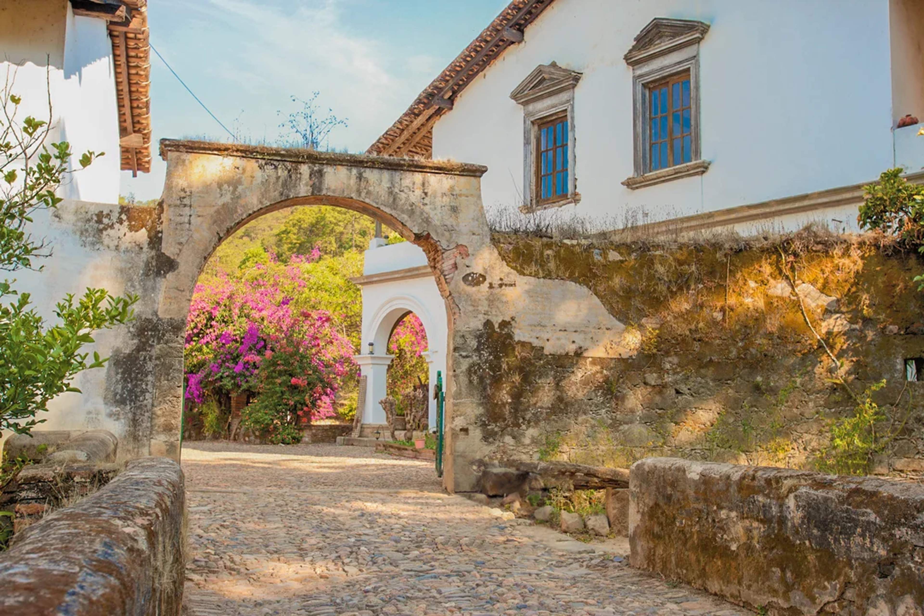 Arco colonial da paso a calles empedradas y flores en un tranquilo pueblo de montaña.
