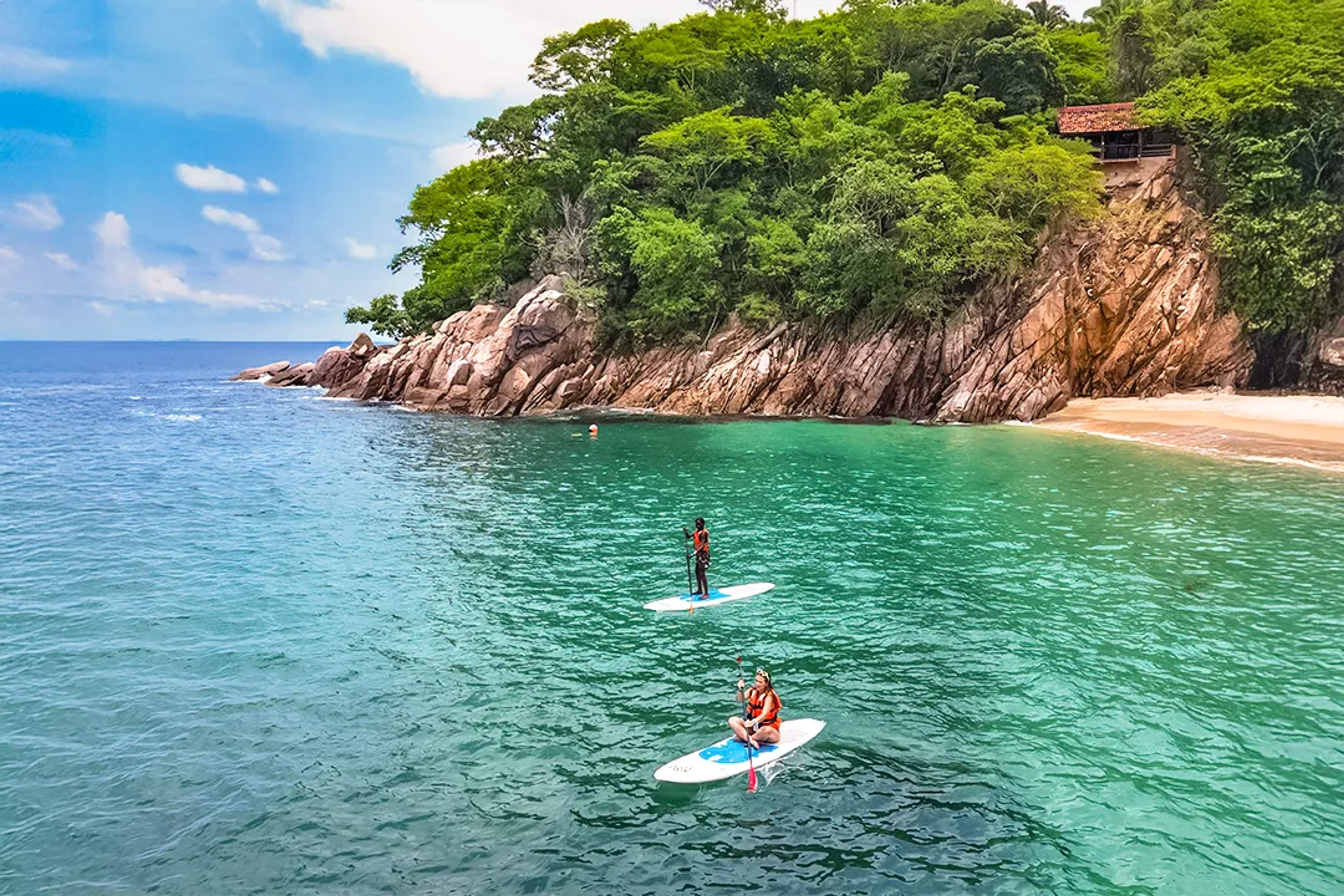 Personas haciendo paddleboard en aguas claras cerca de una playa escondida en Puerto Vallarta con selva y costa rocosa