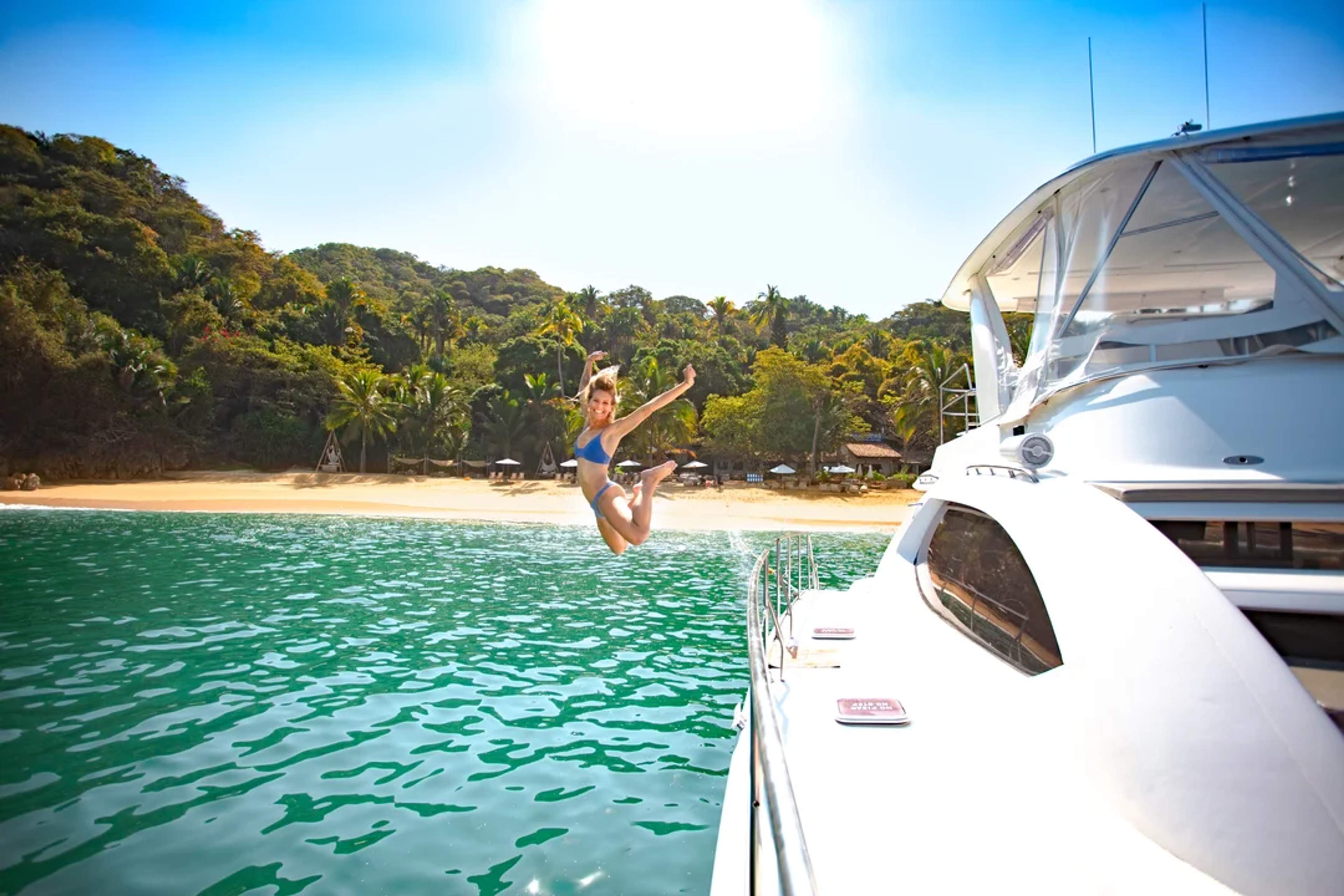 A woman jumps joyfully from a boat into crystal-clear water near a tropical beach paradise.