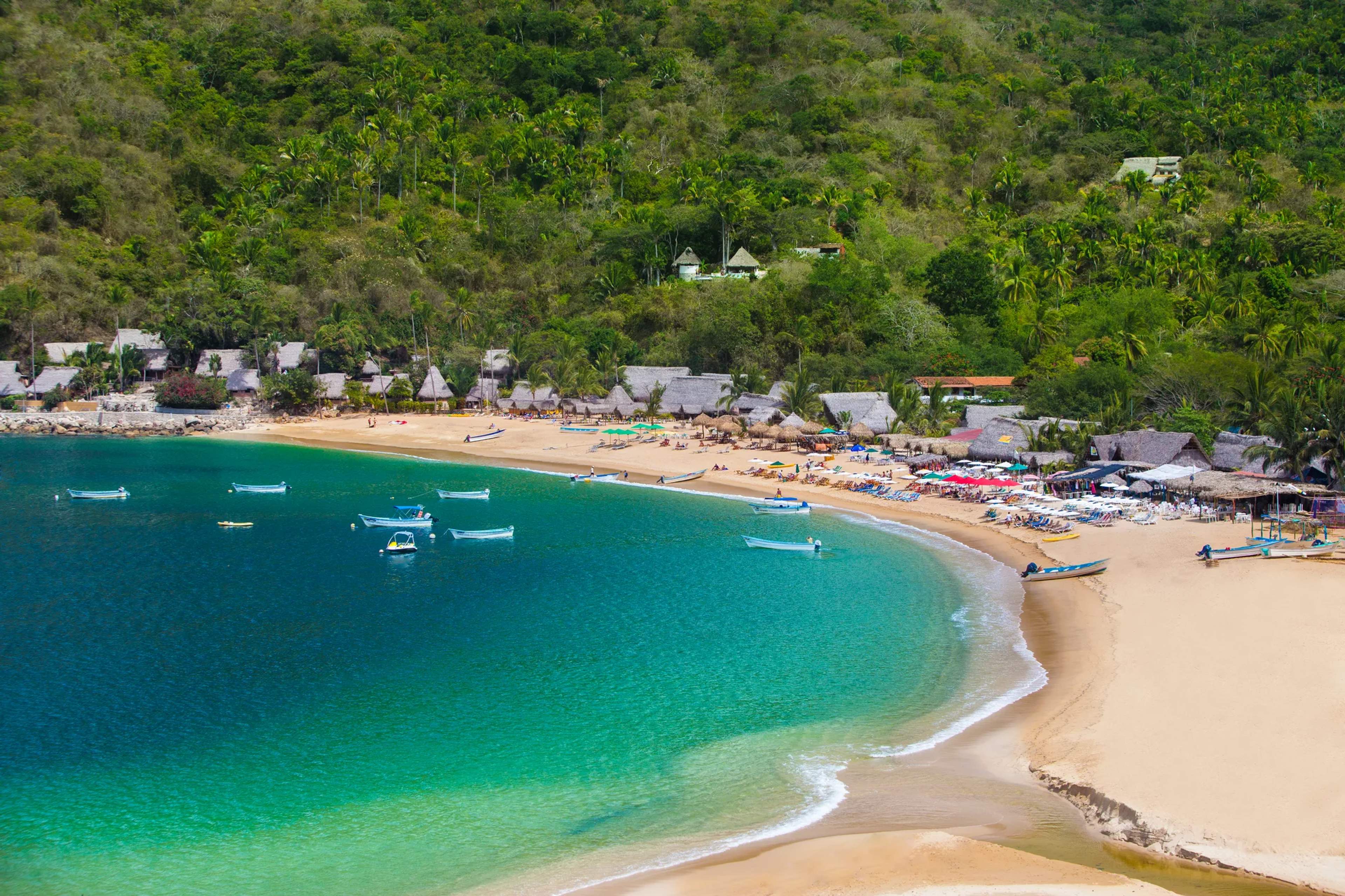 Aerial view of Yelapa's secluded beach cove with turquoise waters, anchored boats, and jungle-backed village on the Pacific
