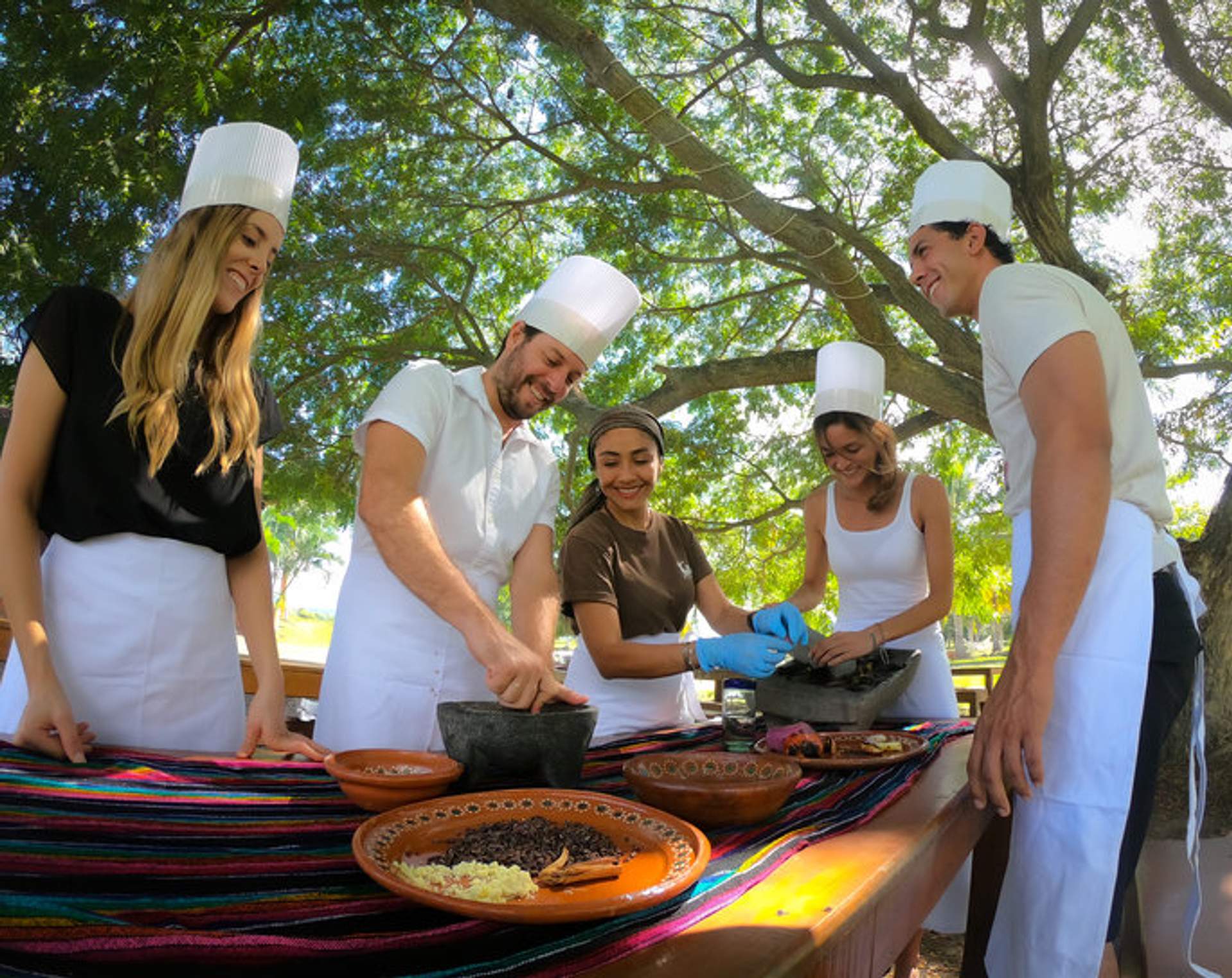 Un grupo de personas participa en una clase de cocina durante un tour de Pueblos con Vallarta Adventures, preparando platillos tradicionales mexicanos.