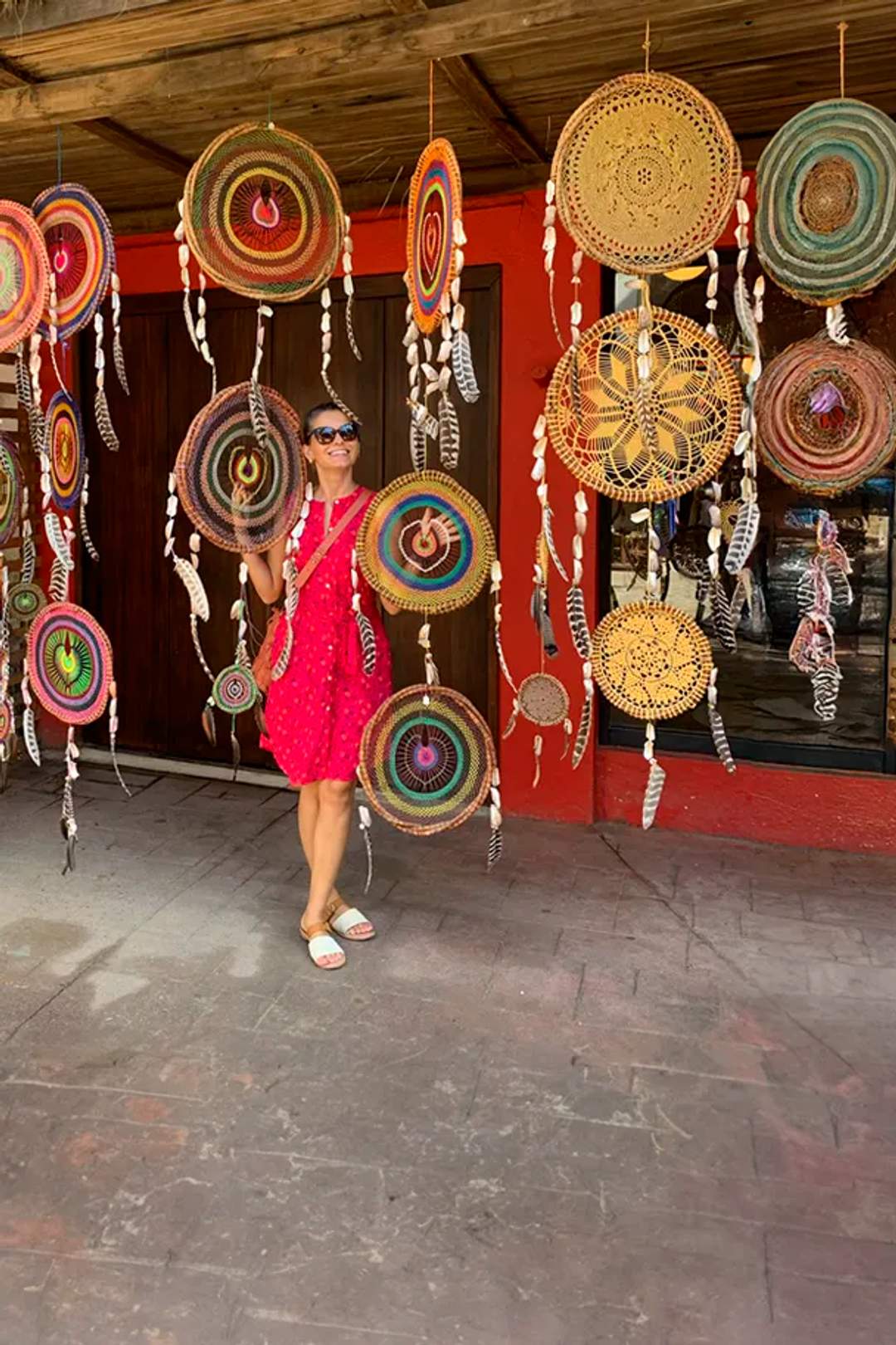 Mujer sonriente entre atrapasueños hechos a mano y coloridos en Sayulita, como parte de un tour de compras en Sayulita.