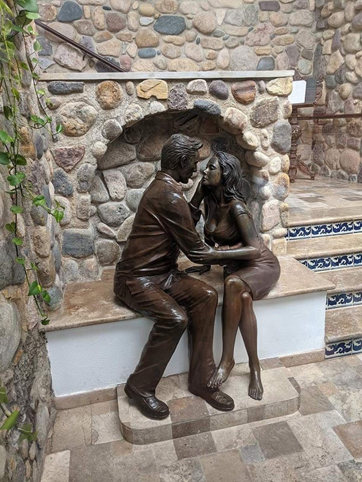 Escultura de Elizabeth Taylor y Richard Burton en un íntimo abrazo, ambientada en un entorno de piedra rústica.