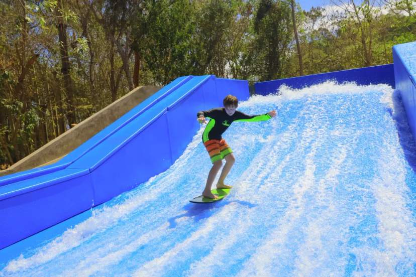 Joven practicando flowboard en una ola artificial en Las Caletas Adventure Park, rodeado de selva tropical.