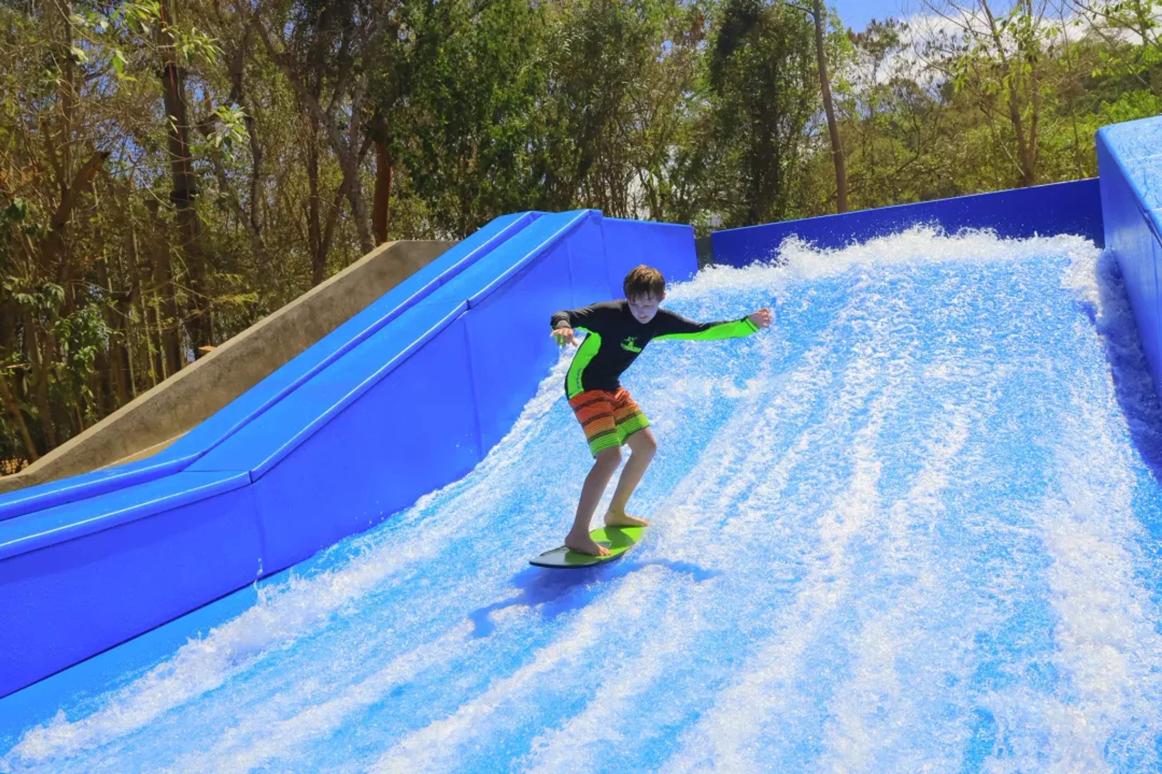Joven practicando flowboard en una ola artificial en Las Caletas Adventure Park, rodeado de selva tropical.