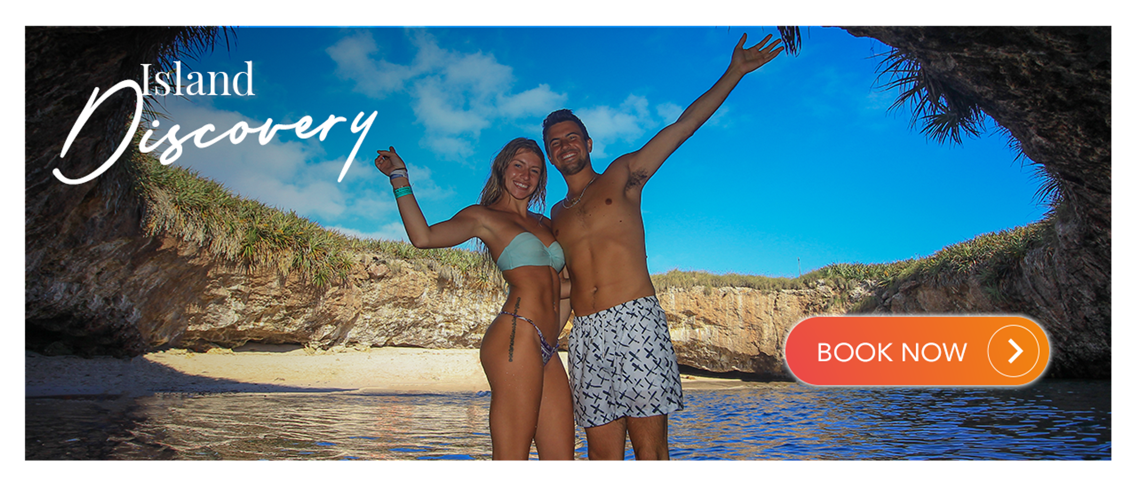 A couple in swimsuits stands on a beach inside a rocky cove.