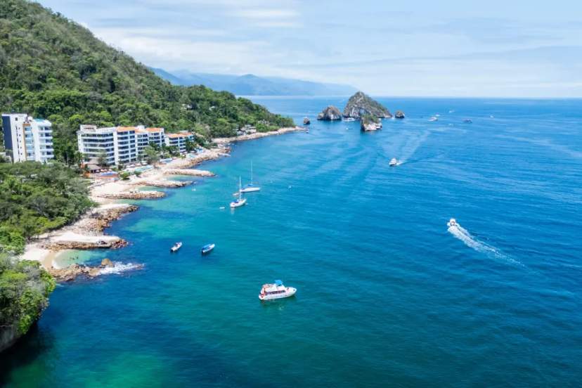 Aerial view of Puerto Vallarta's turquoise coastline with beachfront resorts, lush jungle cliffs, and boats anchored in the