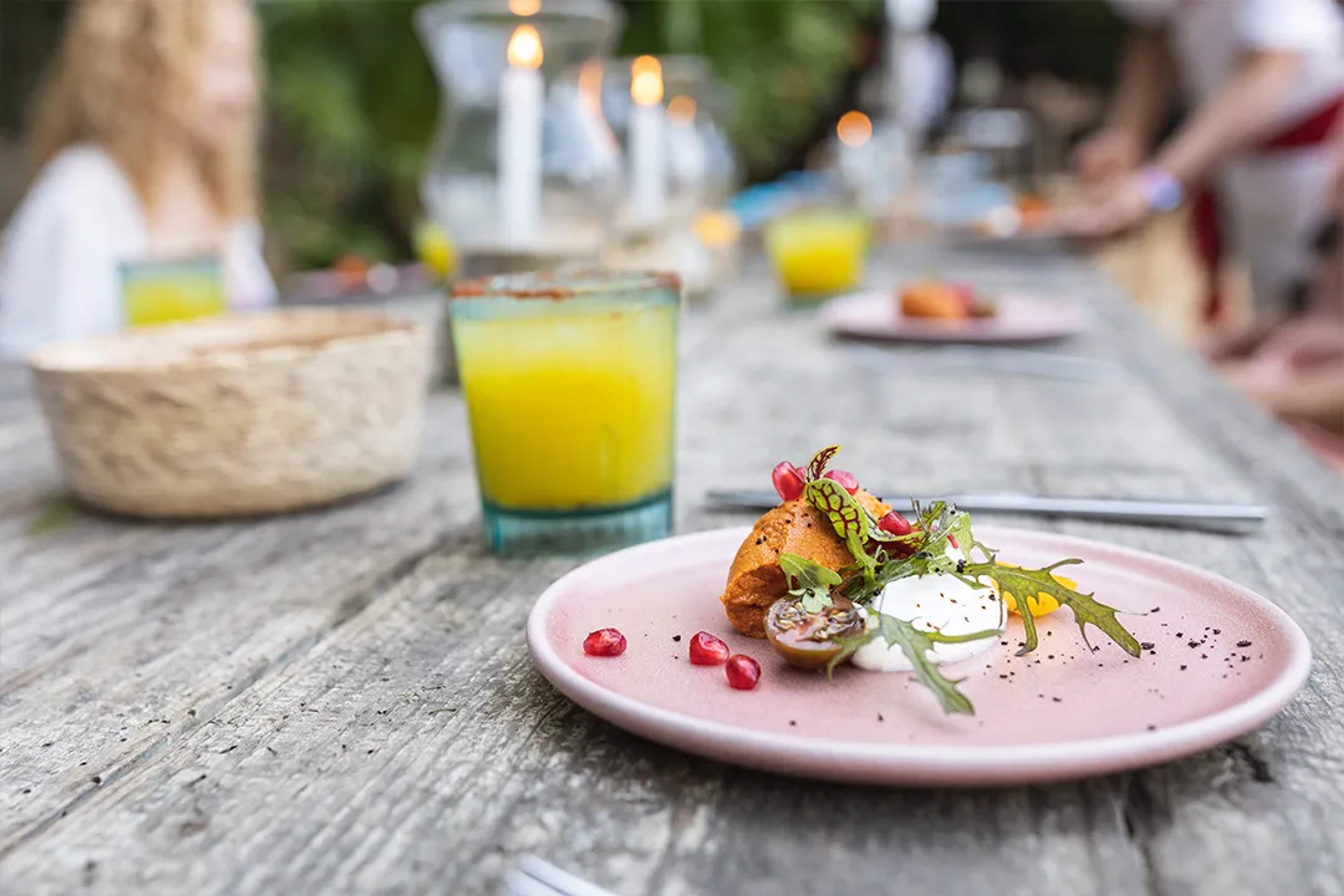 Elegant gourmet dish and cocktail served on a rustic outdoor table with candlelight.