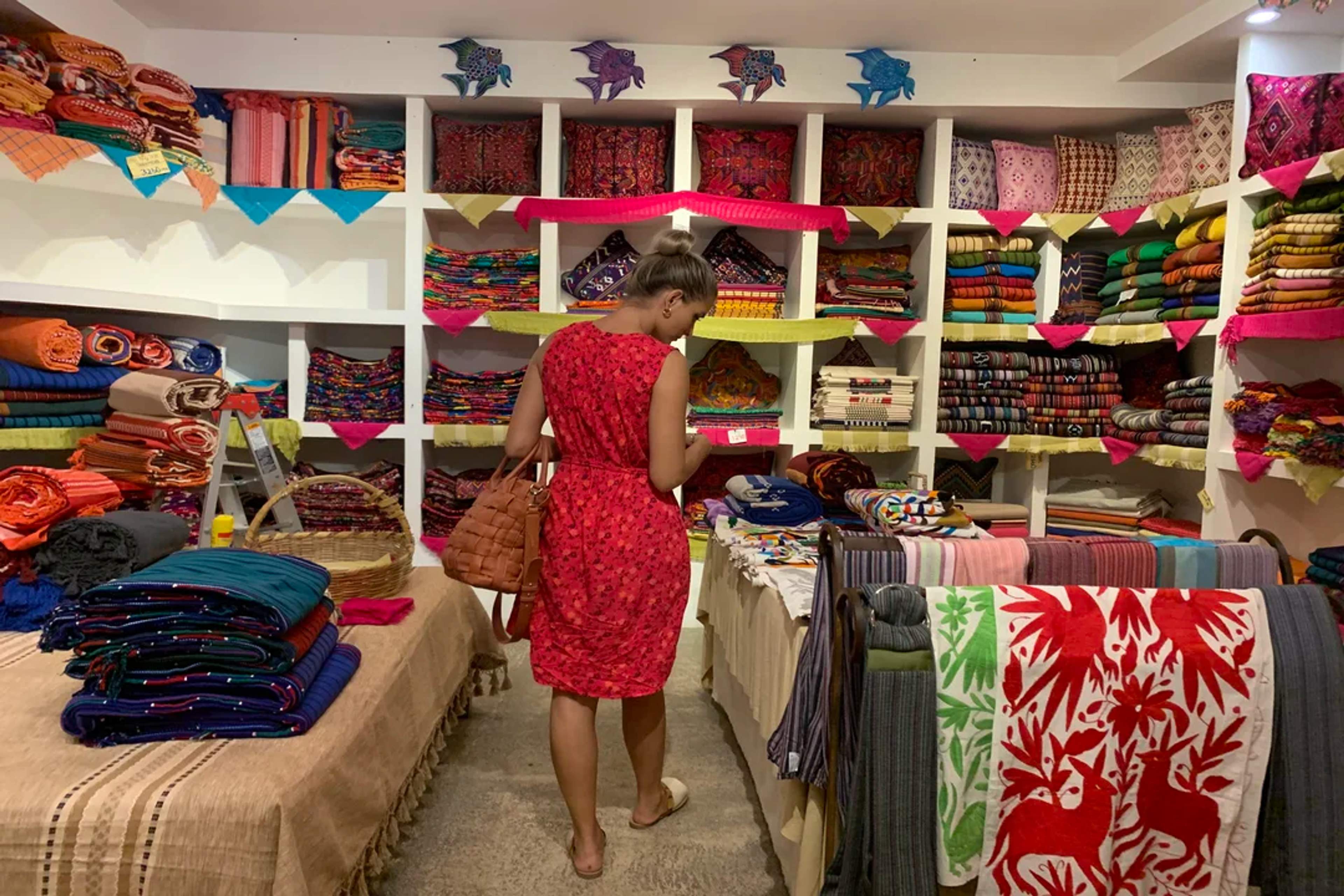 Woman explores a colorful textile shop filled with handmade Mexican fabrics and vibrant patterns.