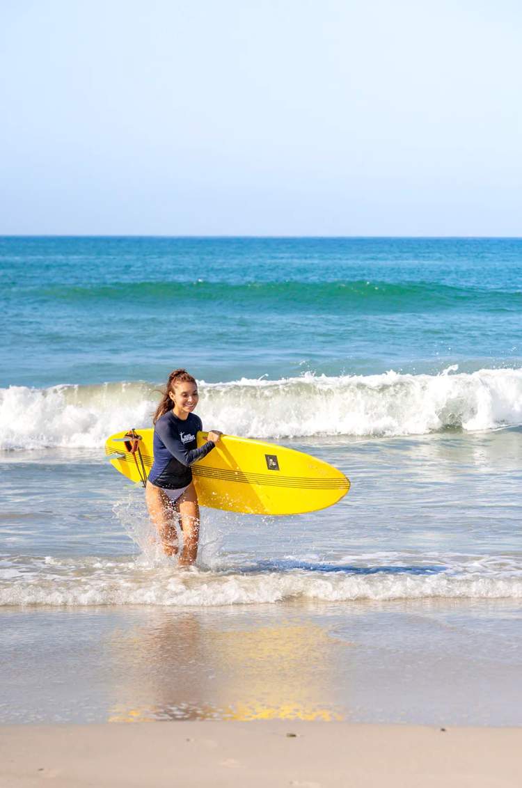 Girl carrying a surfboard after a private surf lesson on Punta Mita Beach, with Vallarta Adventures