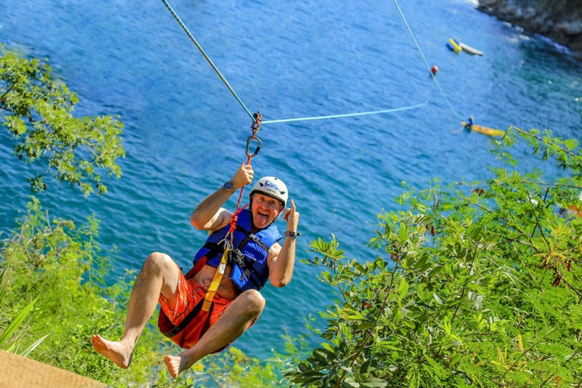 A man enjoying a thrilling zipline ride over the ocean at Las Caletas Beach, smiling and giving a thumbs-up.