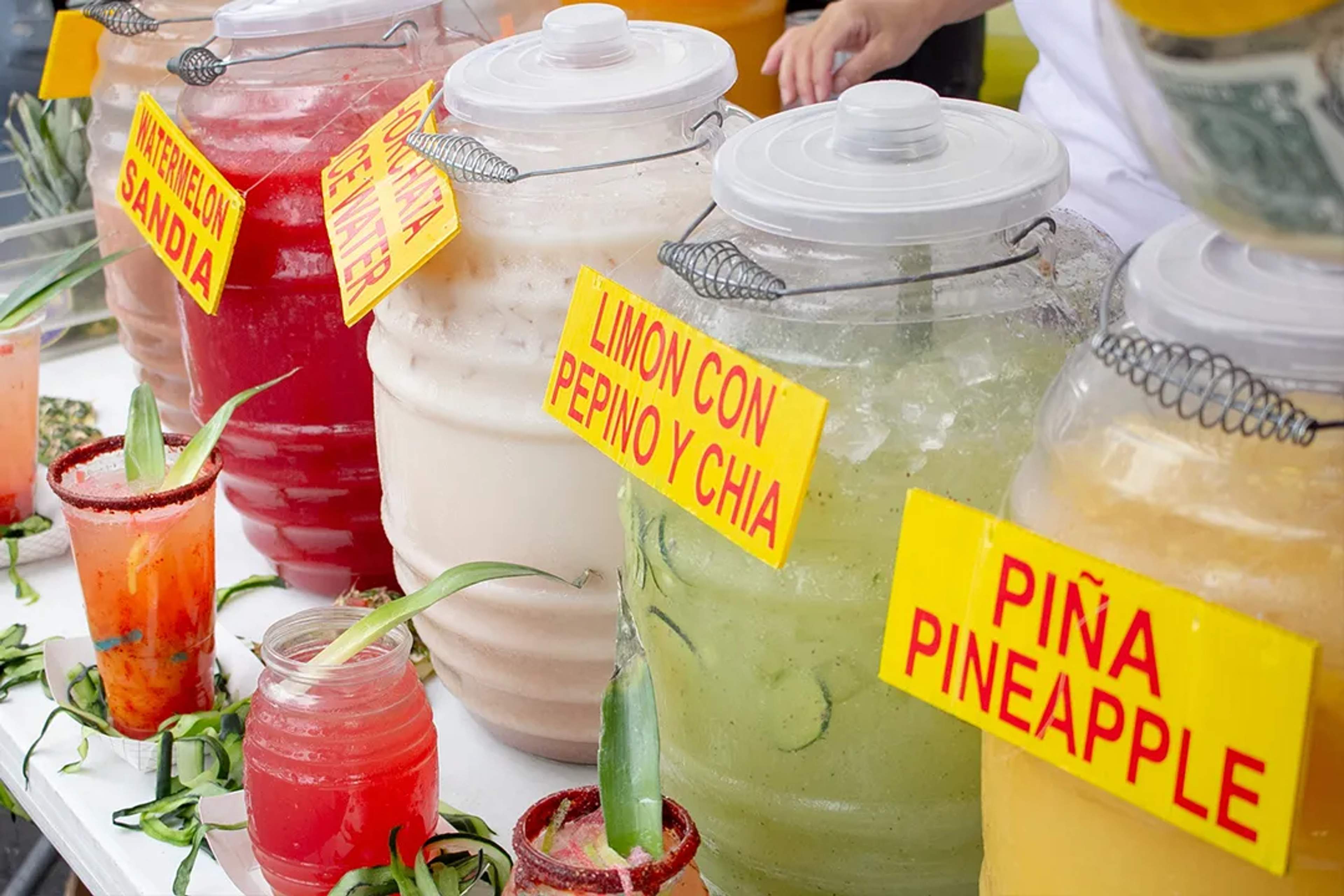 Coloridas aguas frescas en vitroleros con sabores como sandía, horchata, limón y piña.