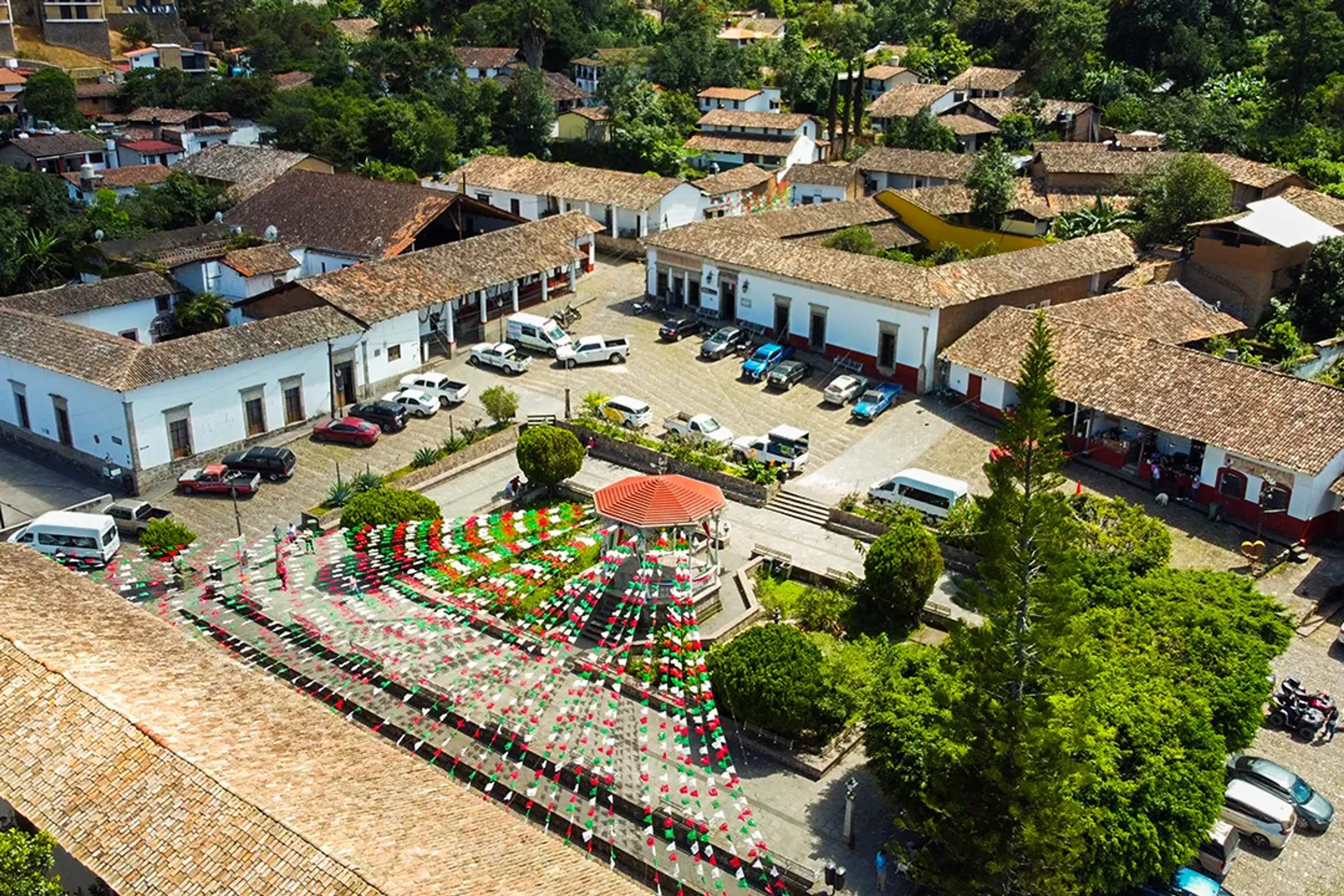 Aerial view of San Sebastián del Oeste main square, colonial rooftops, gazebo and Mexican flags mountain town