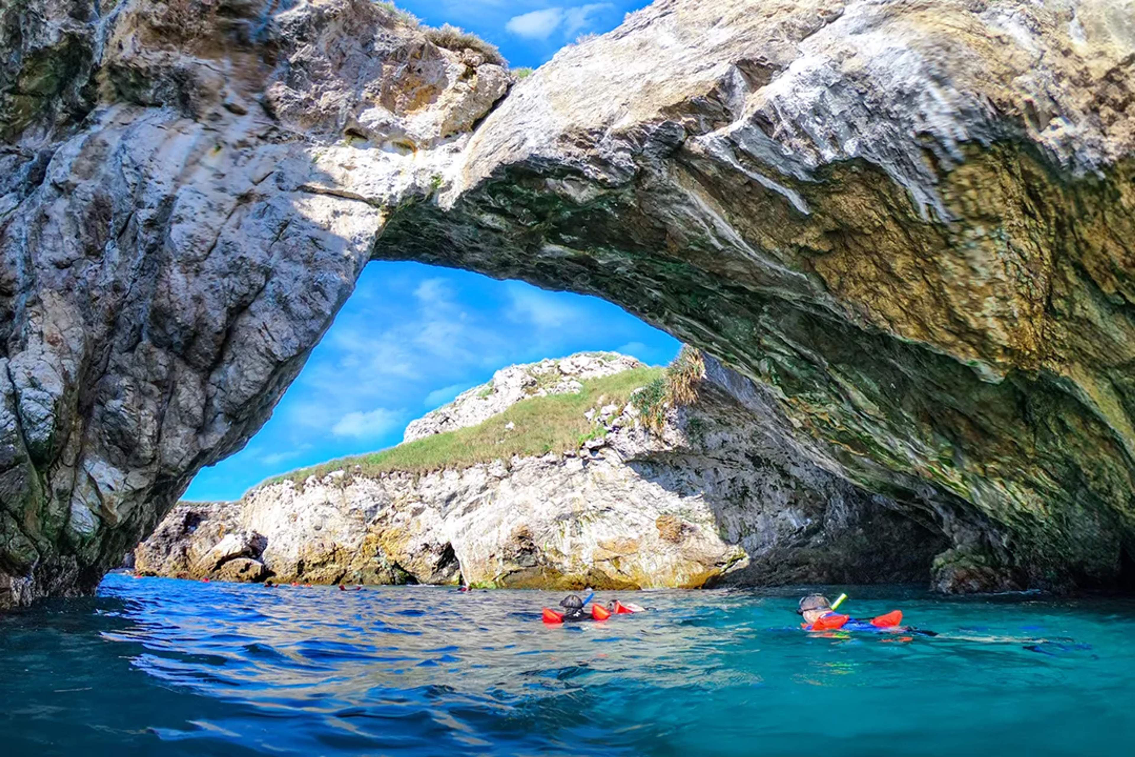 Snorkelers swim through crystal waters under a rocky arch at the Marietas Islands.