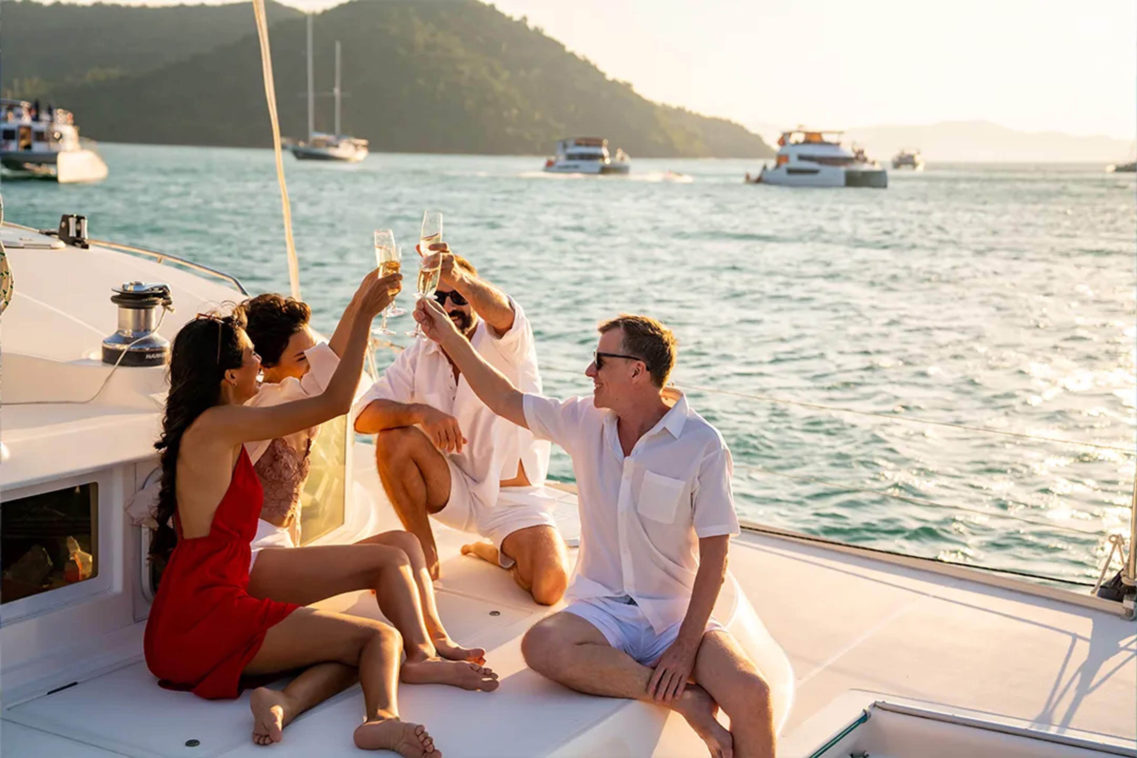 Friends toast with champagne on a yacht at sunset, surrounded by calm sea and boats.