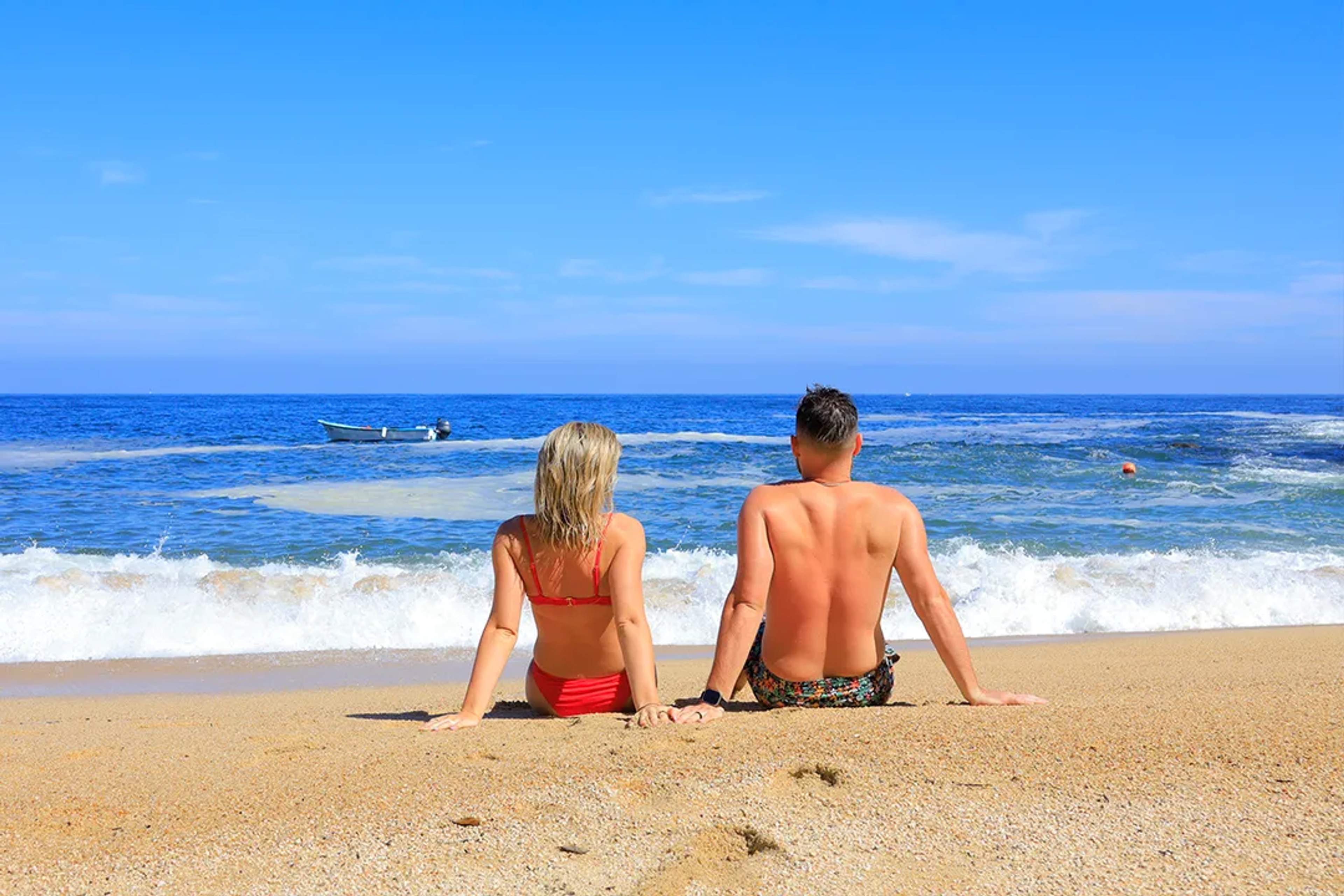 Couple relaxing on a sunny beach, sitting by the ocean waves and enjoying a peaceful seaside moment together