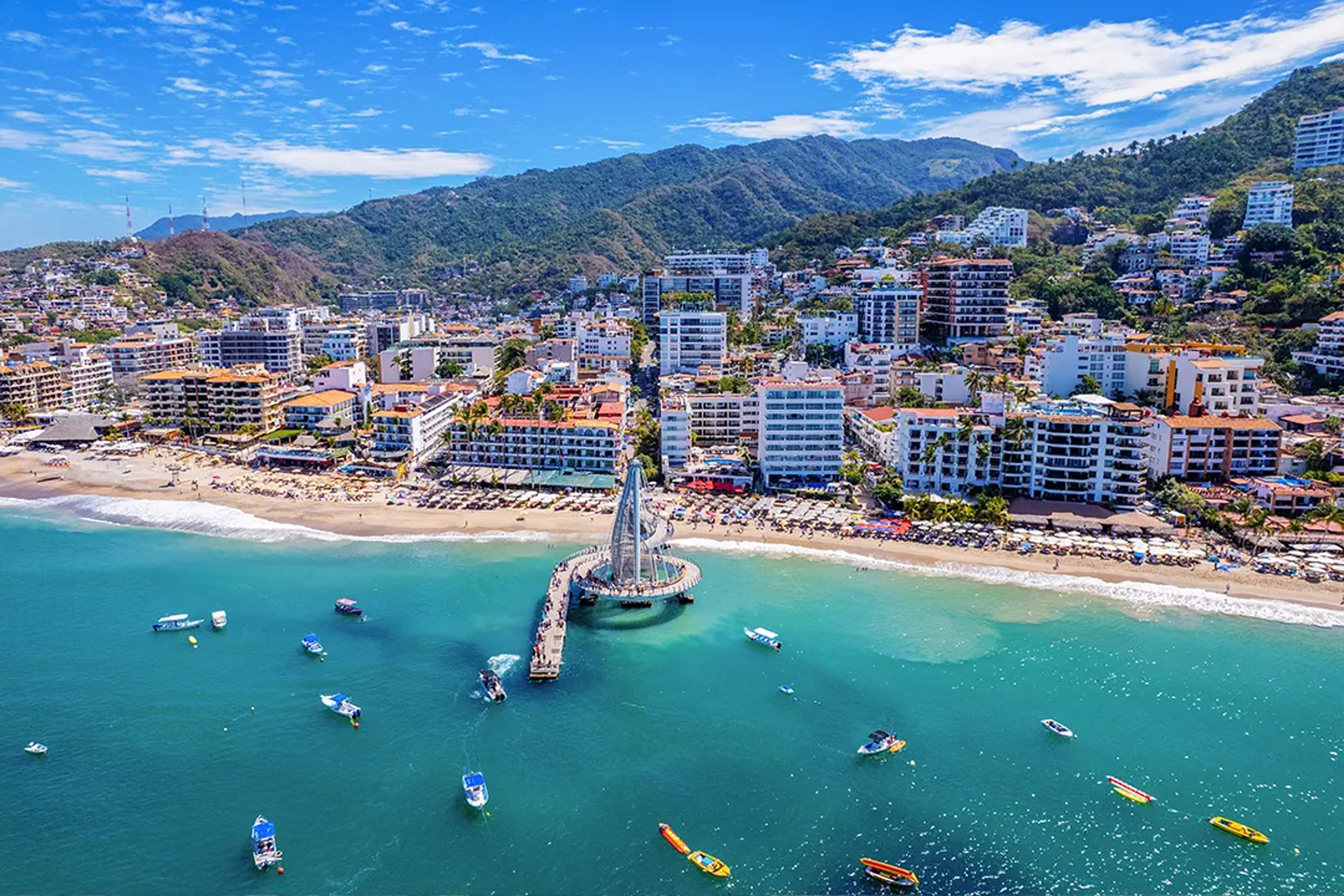 Aerial view of Puerto Vallarta coastline with Los Muertos Pier, beach, boats, and Sierra Madre mountains