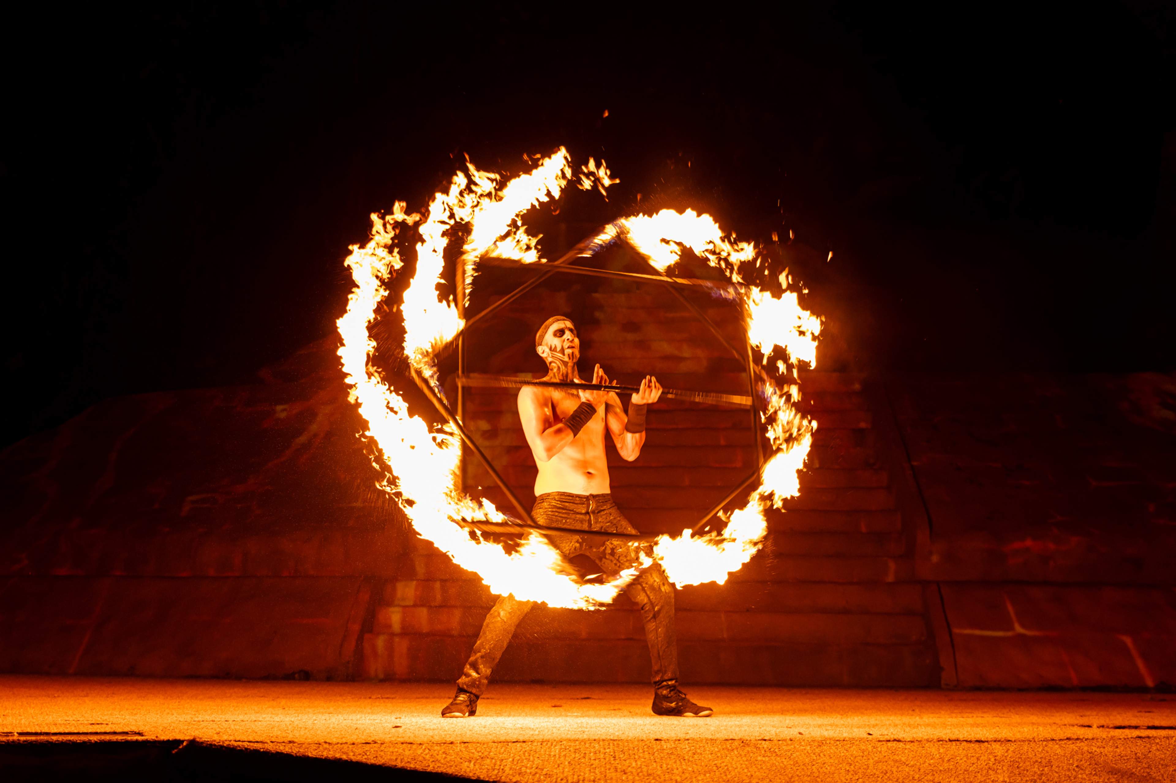 A fire performer creating a mesmerizing display with a flaming hoop, against a dark background during a nighttime show.