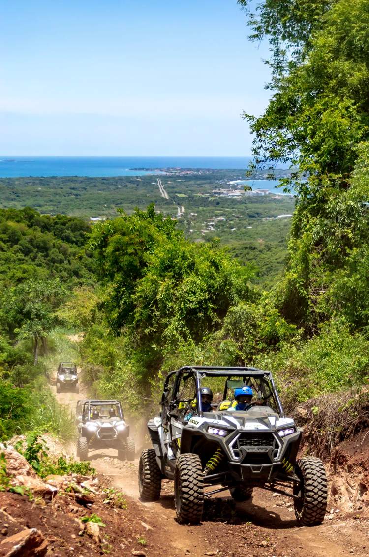 Vehículos todoterreno conduciendo por un sendero de selva tropical con el mar de fondo.