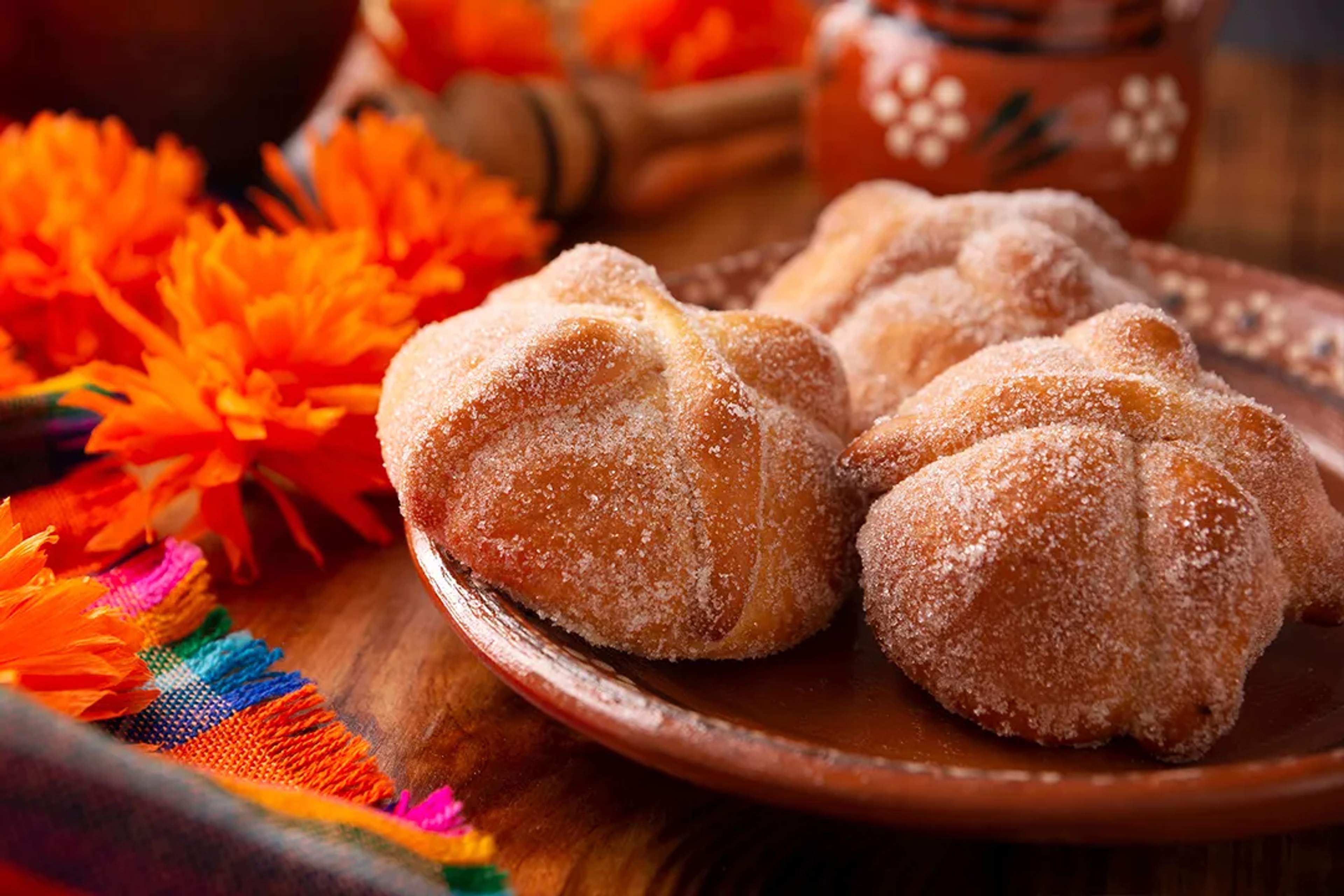 Pan de muerto con azúcar en plato de barro, rodeado de cempasúchil para Día de Muertos.