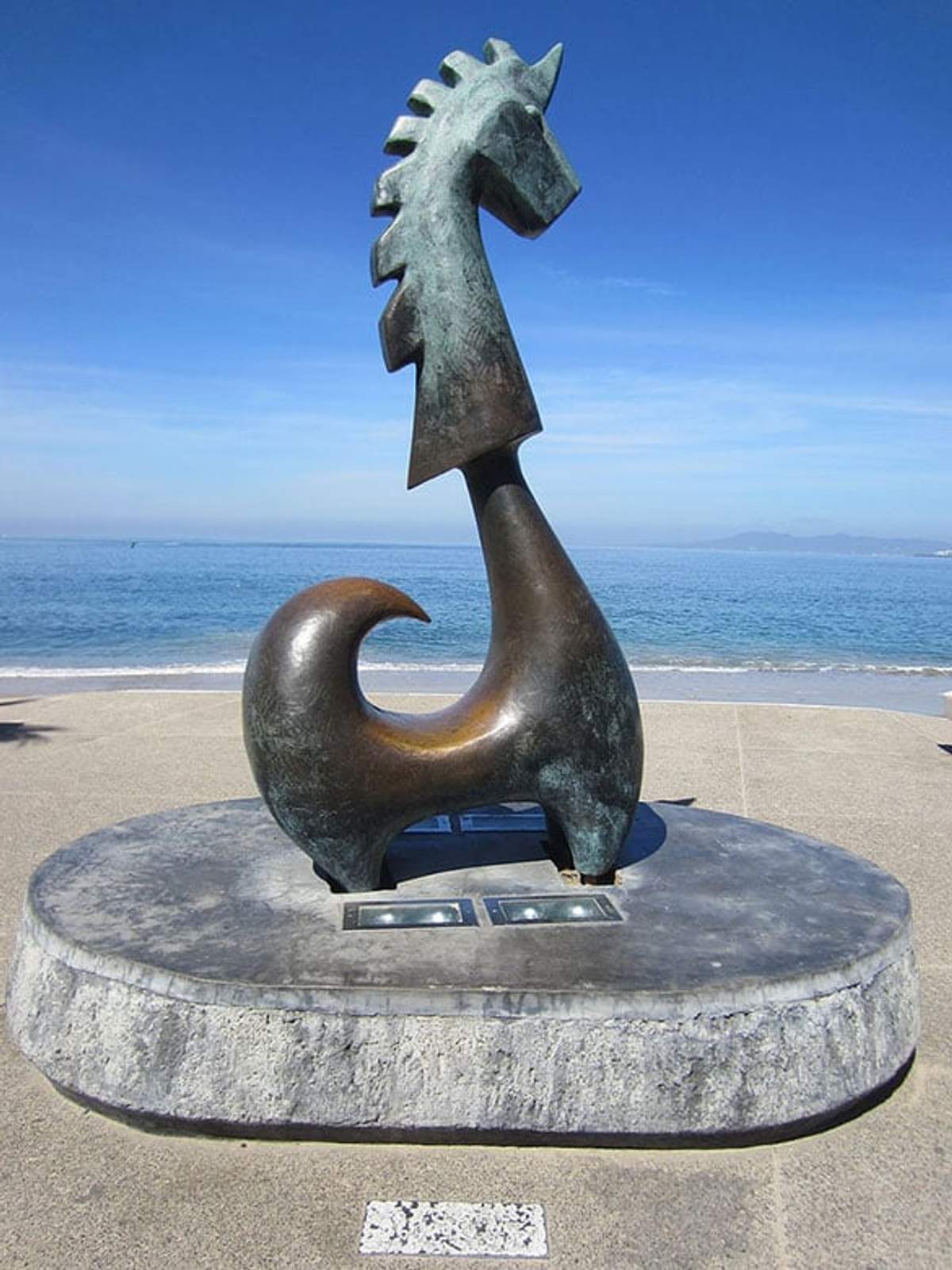 Escultura de unicornio estilizado en el malecón de Puerto Vallarta, con vista al mar y cielo despejado de fondo.