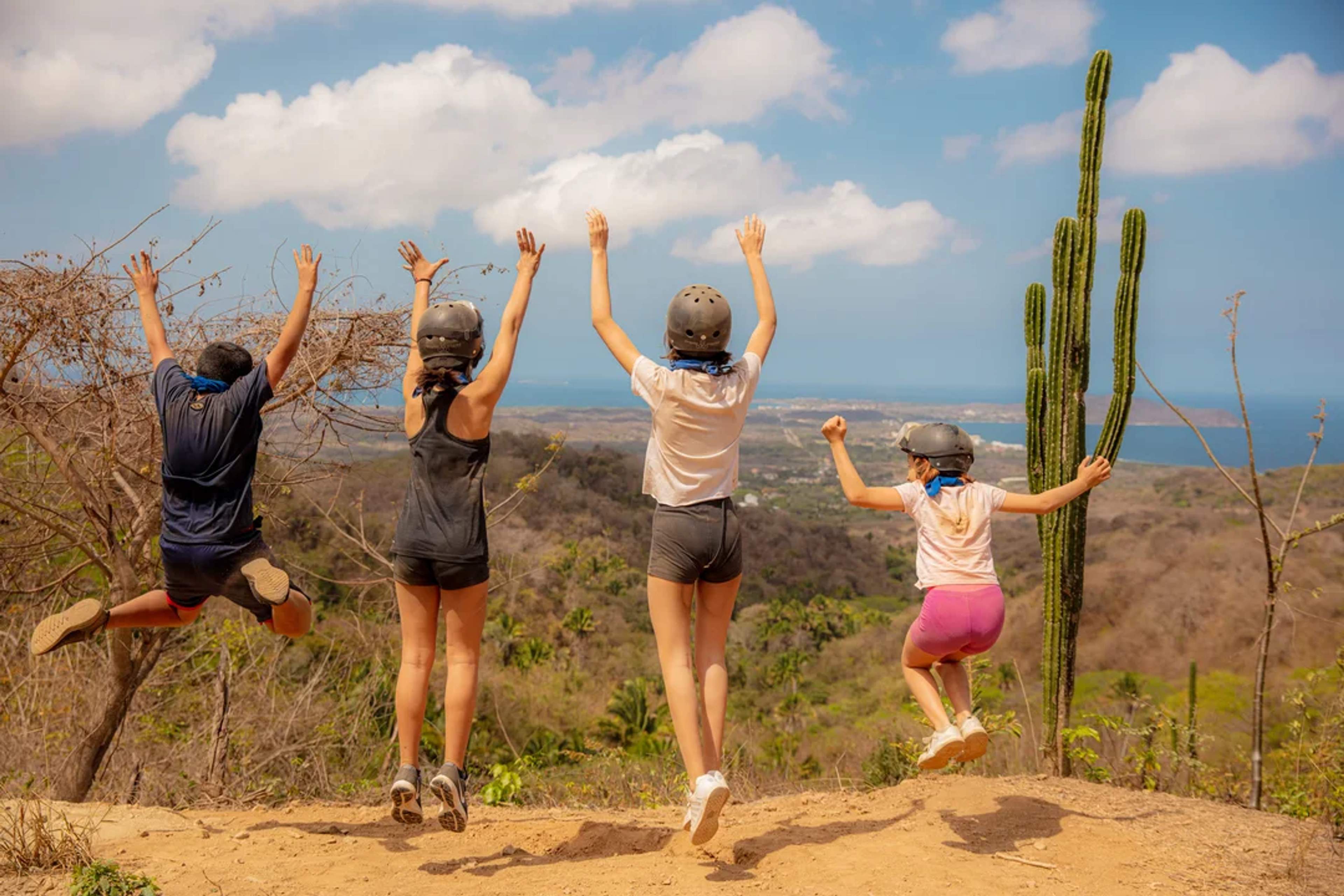 Niños saltan felices en una cima escénica con vista al mar y al paisaje del desierto.