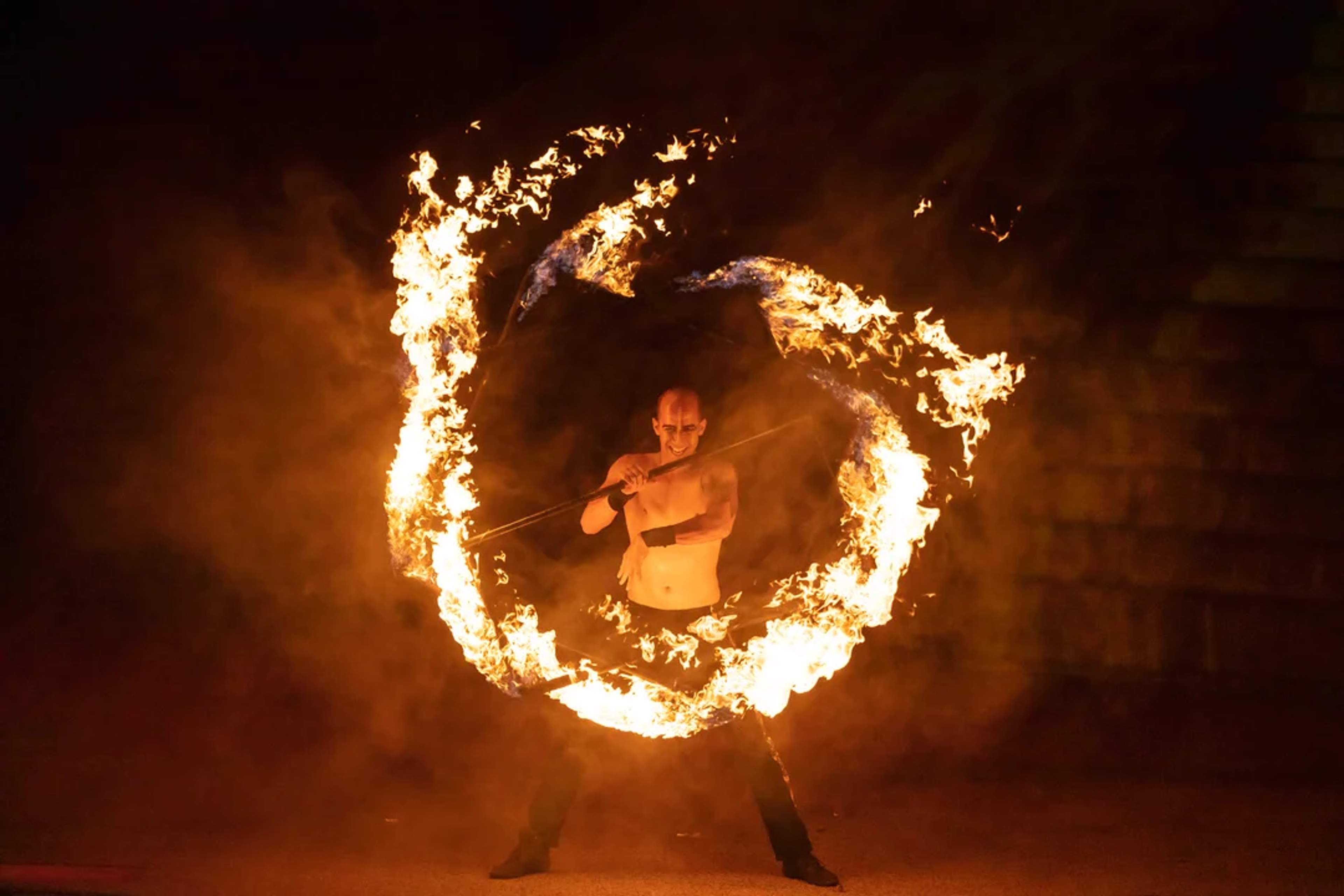 A fire performer spins a flaming staff, creating a mesmerizing circle of fire against the dark night backdrop.
