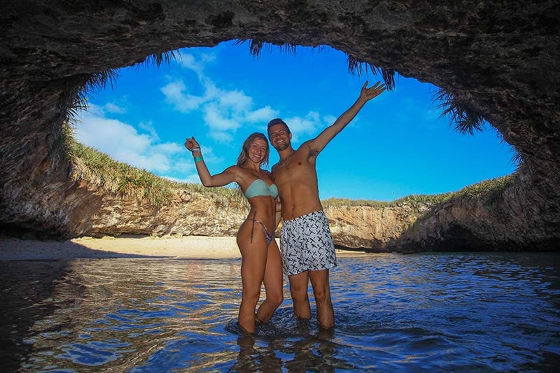 Una pareja sonriente se encuentra en el agua bajo el arco de roca en Playa Escondida, Islas Marietas, México.