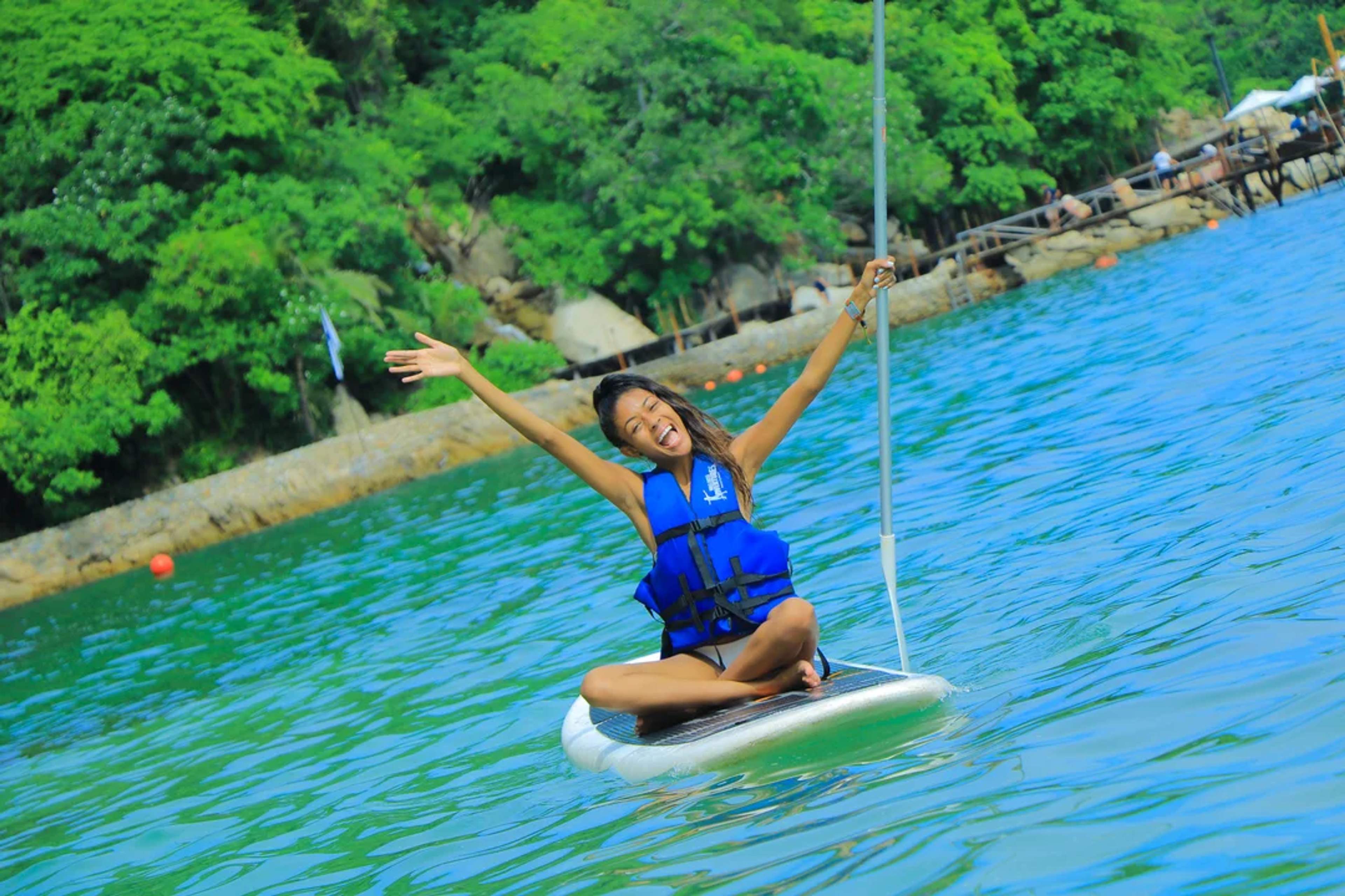 Mujer sonriente disfruta remando sentada en tabla de paddle en aguas tranquilas de Las Caletas.
