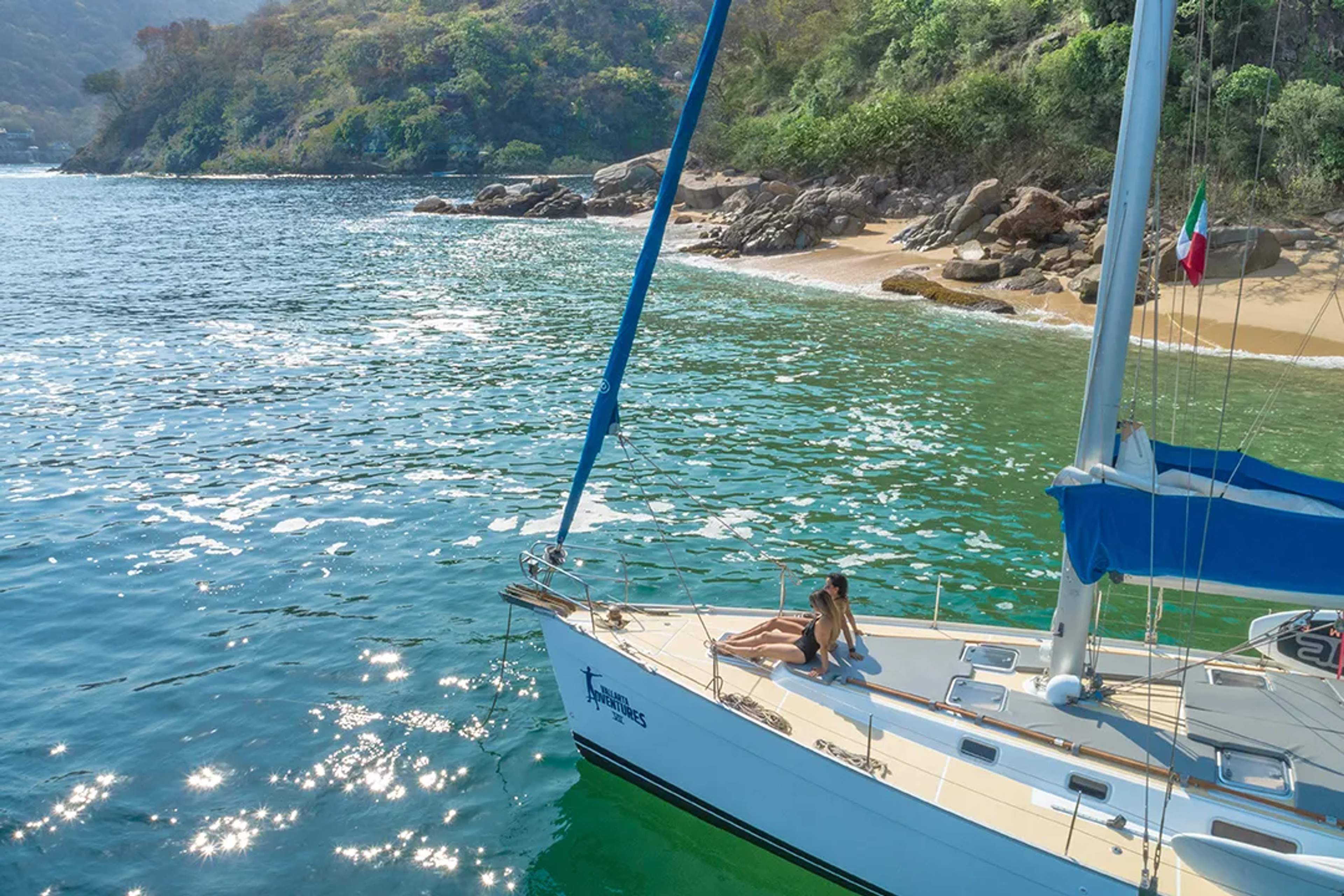 Traveler relaxes on a sailboat deck by a secluded beach with sparkling turquoise waters.
