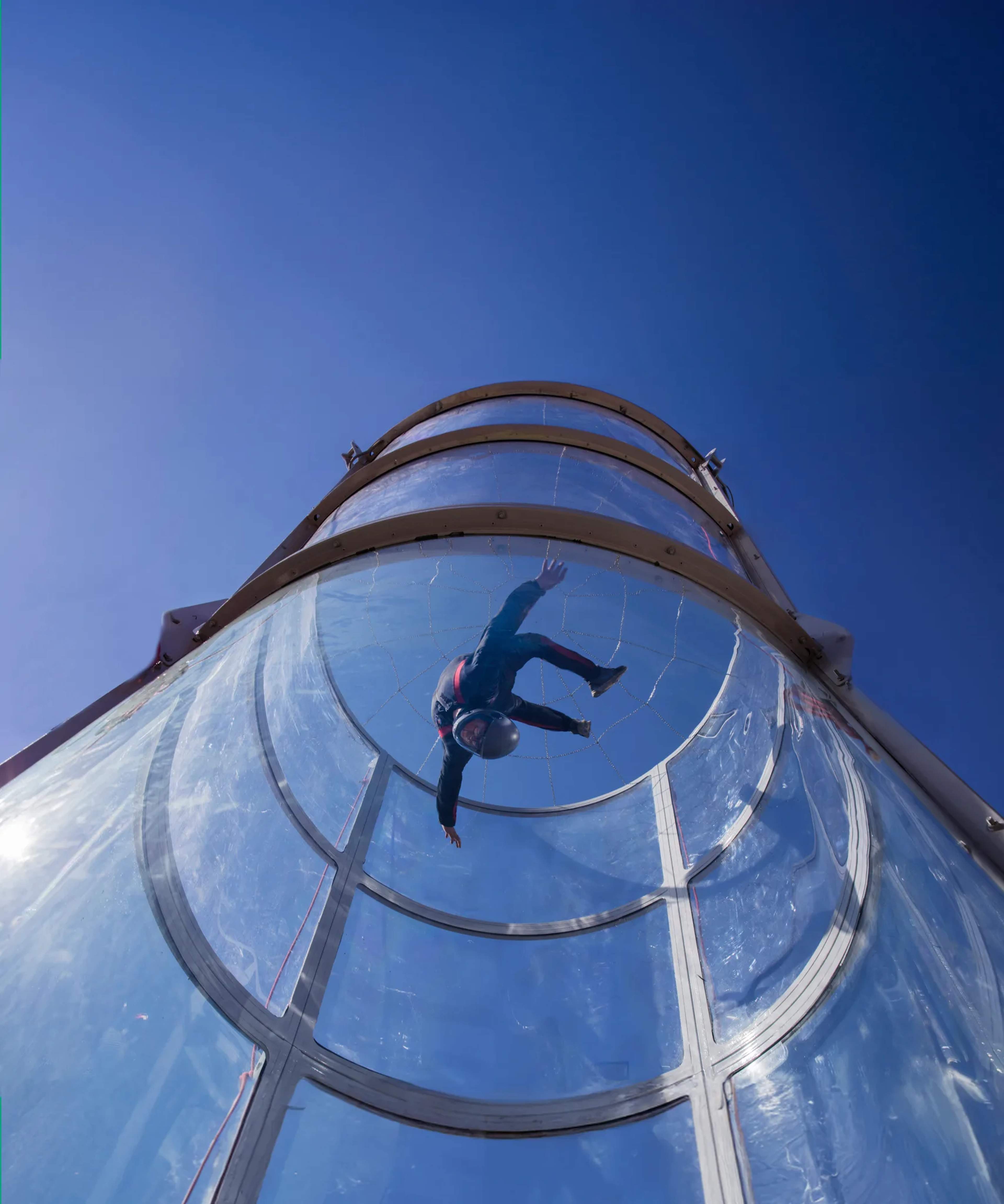 Persona deslizándose por un tubo de tobogán transparente bajo un cielo azul brillante durante una actividad de aventura.