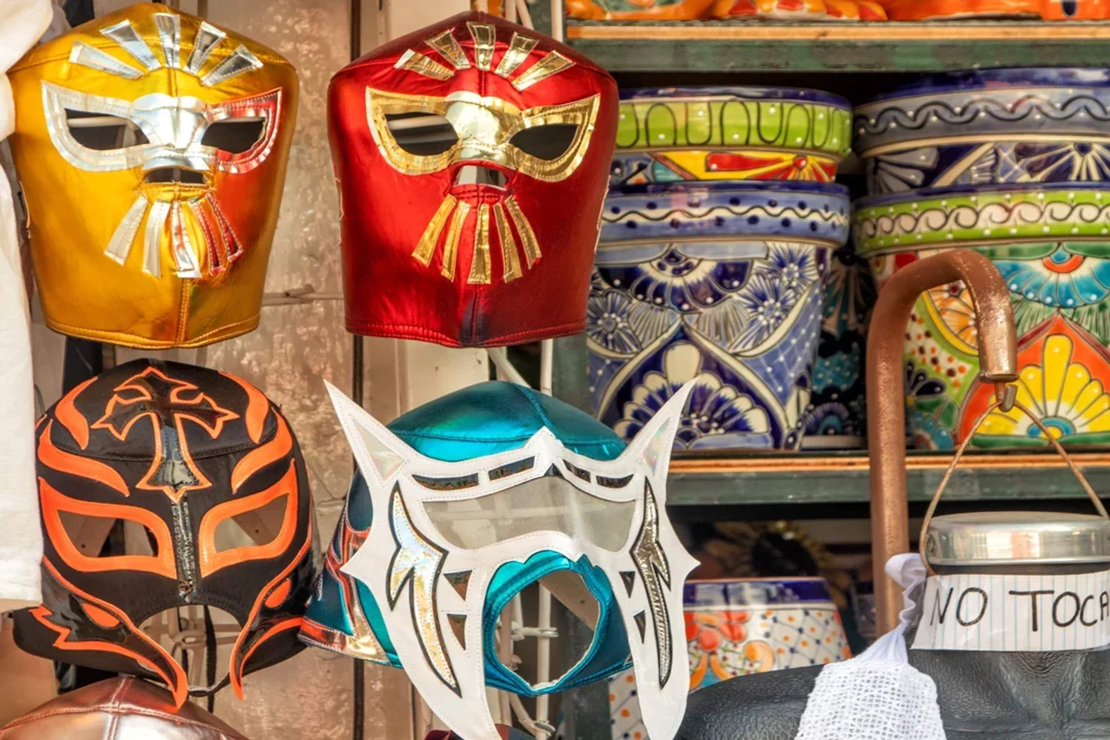 Coloridas máscaras de lucha libre y cerámica mexicana en un puesto de mercado típico.