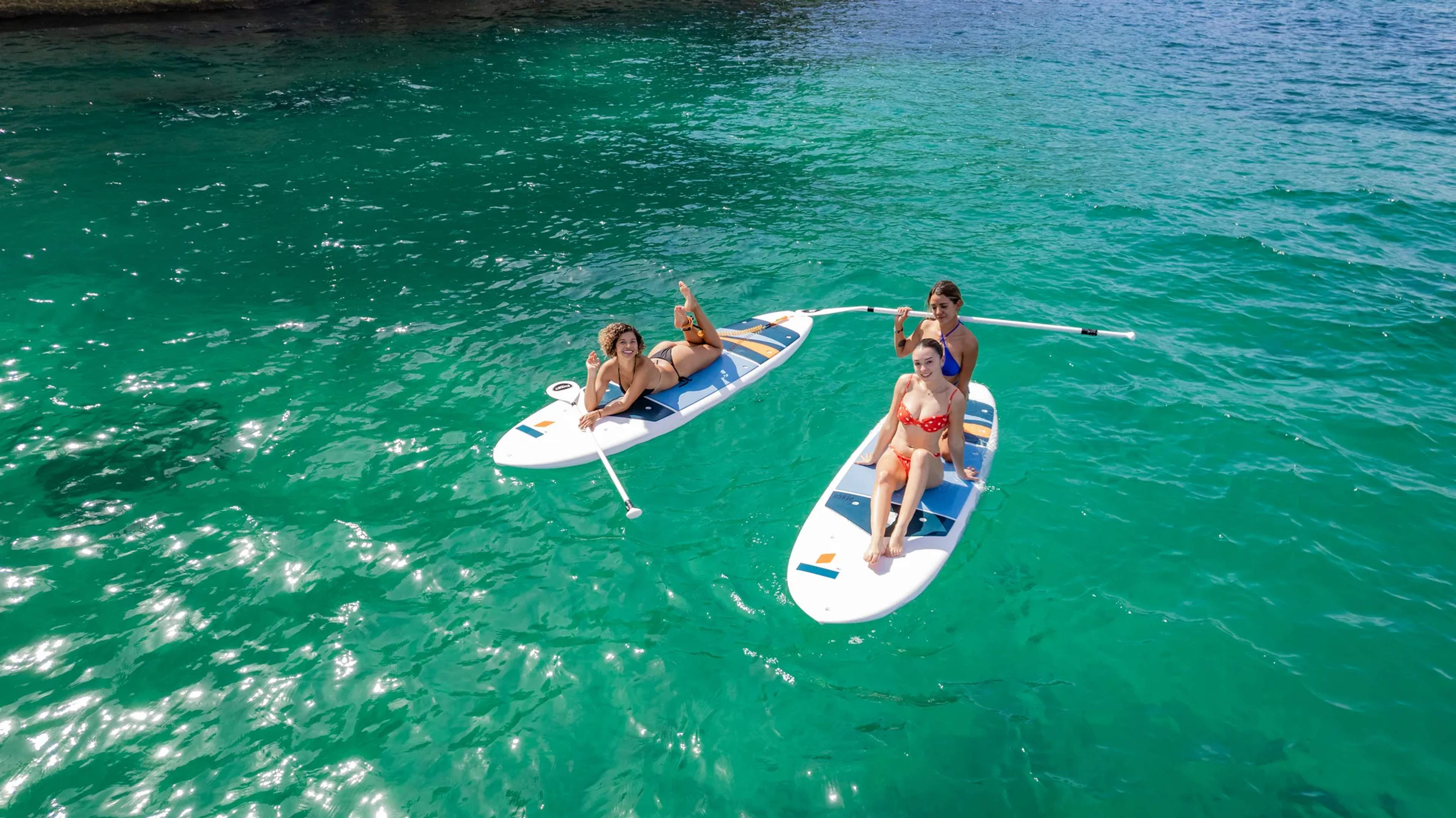 Turistas practican paddleboard en aguas turquesas de la costa mexicana durante una excursión de vela y deportes acuáticos.
