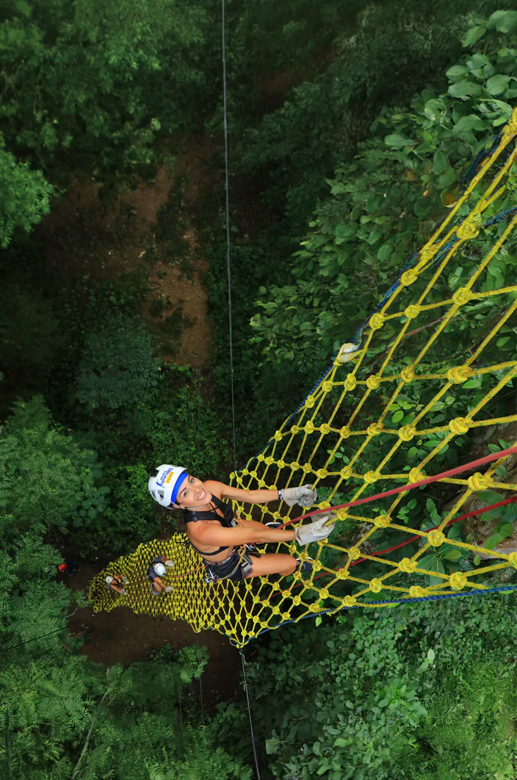 Friends climbing a high net suspended from a tall tree in the middle of the Puerto Vallarta jungle.