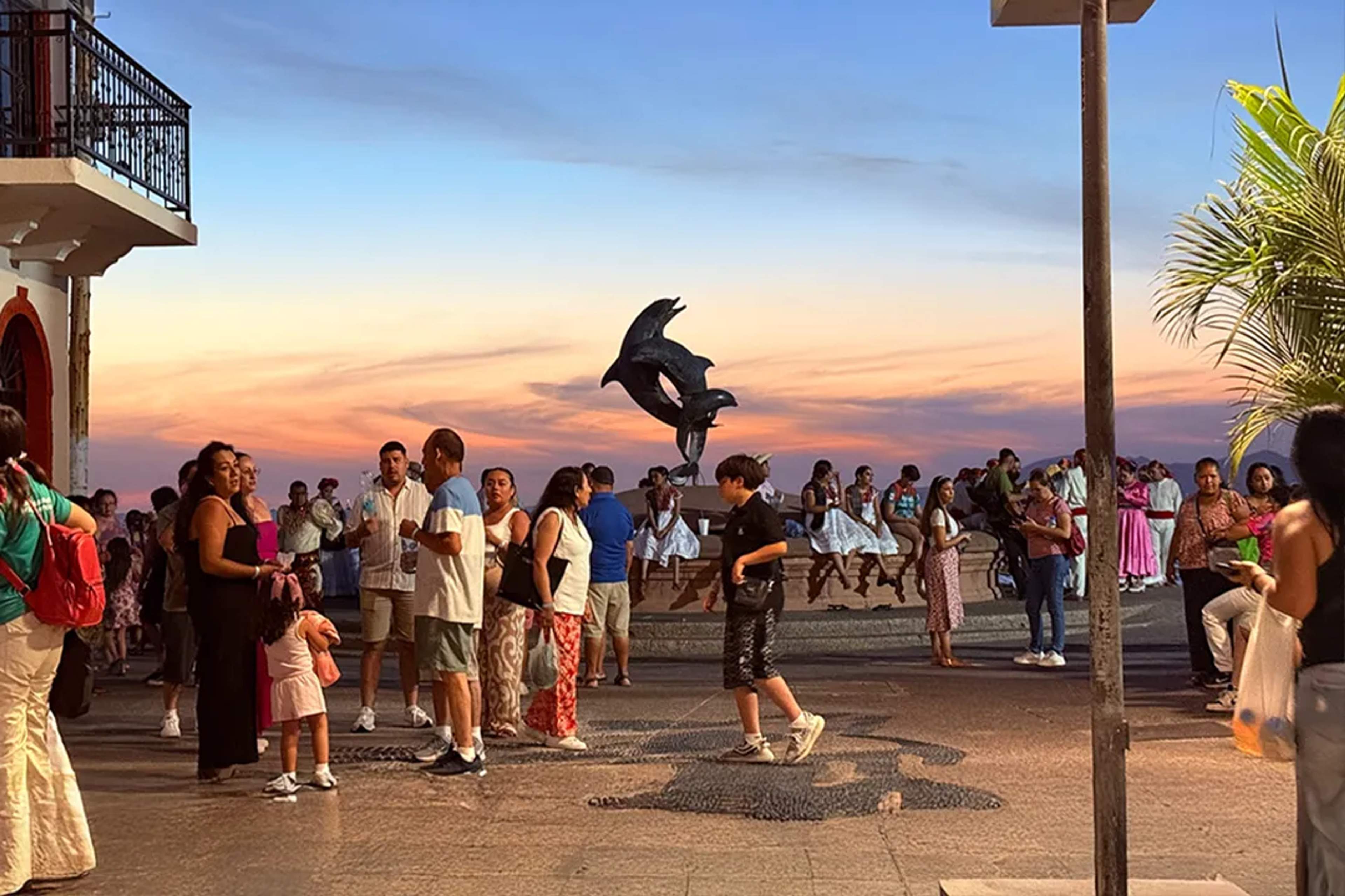 Malecón de Puerto Vallarta al atardecer con visitantes, esculturas icónicas y vibrante vida nocturna