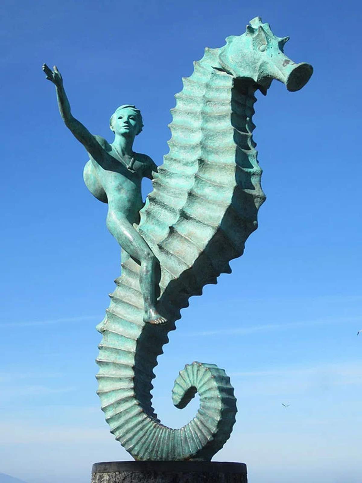 Escultura de niño montando un caballito de mar en Puerto Vallarta, con cielo azul despejado de fondo.