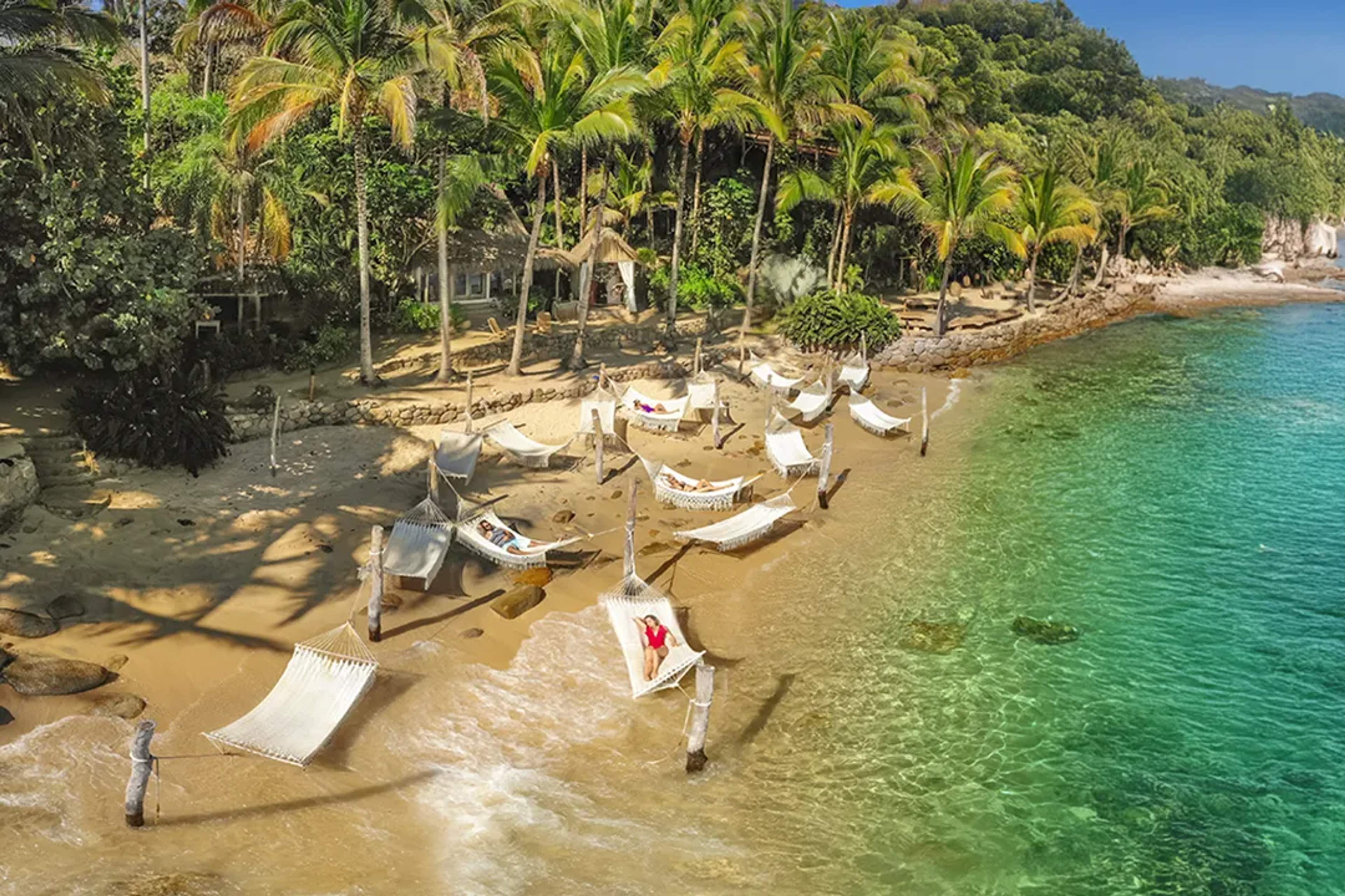 Hammocks on a tropical beach at Las Caletas in Puerto Vallarta with palm trees and clear turquoise water