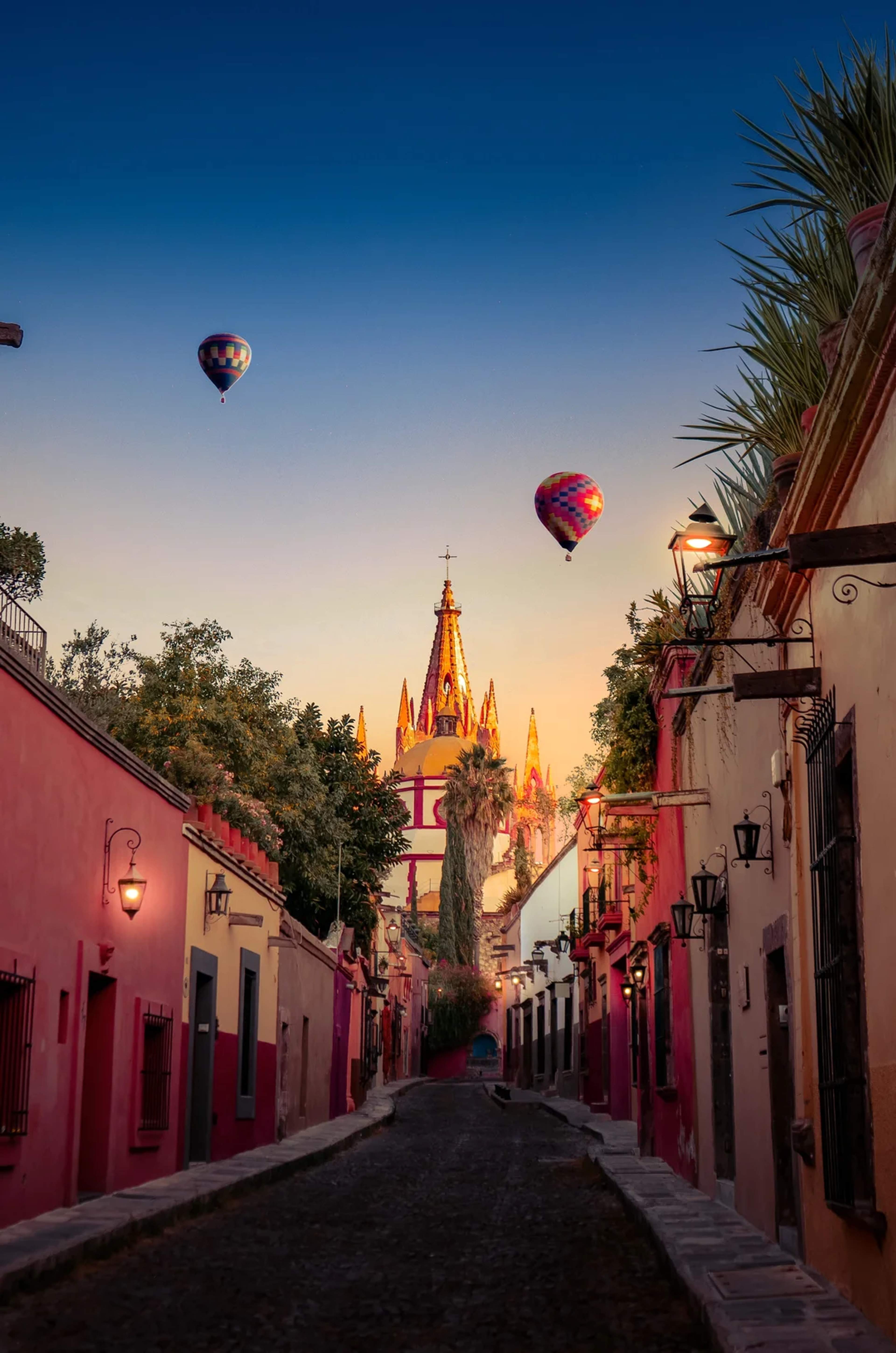A charming street in San Miguel de Allende at sunrise, with hot air balloons floating above the church.