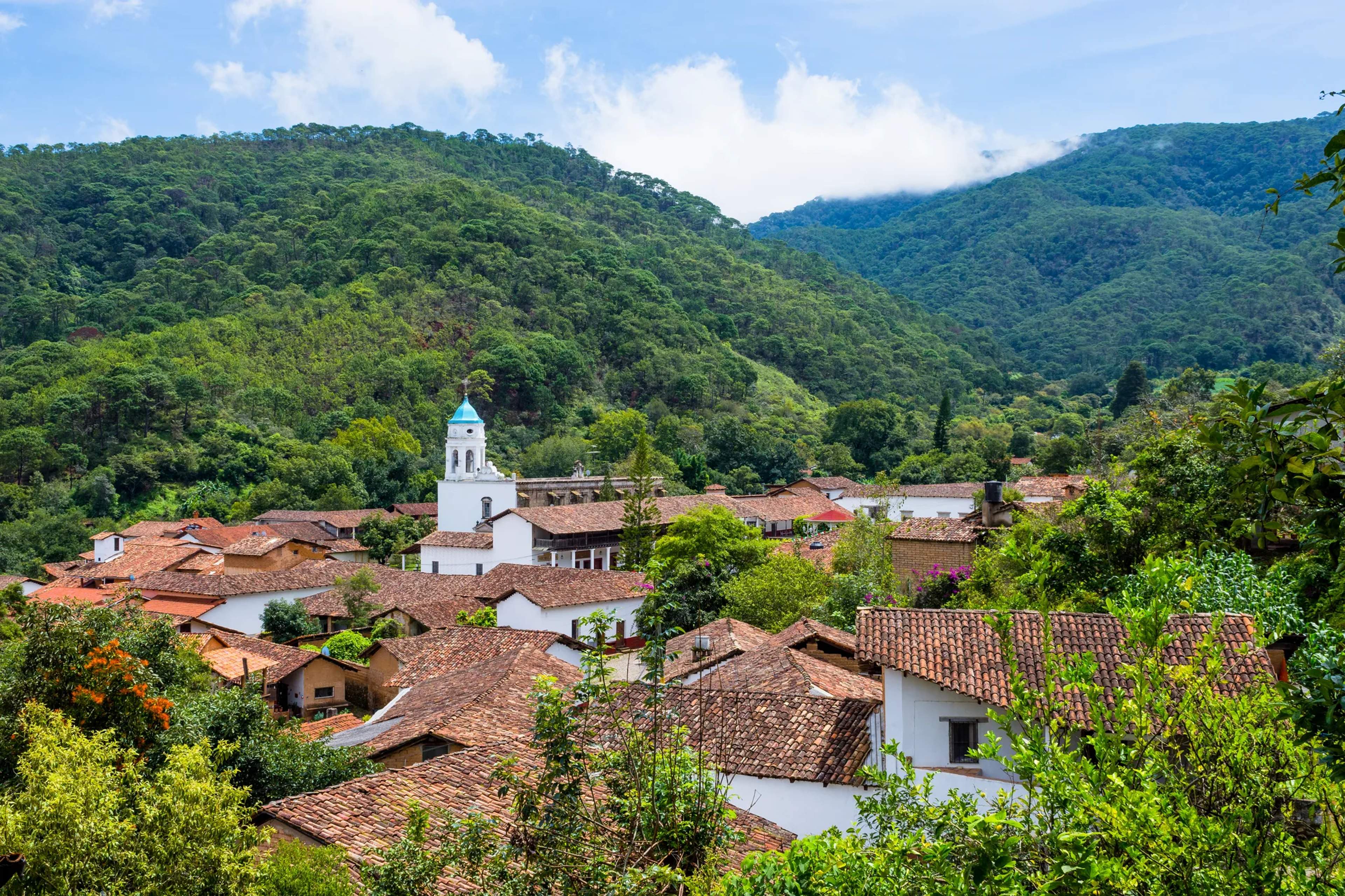 Iglesia colonial de campanario blanco sobre San Sebastián del Oeste, rodeado de verdes valles montañosos.