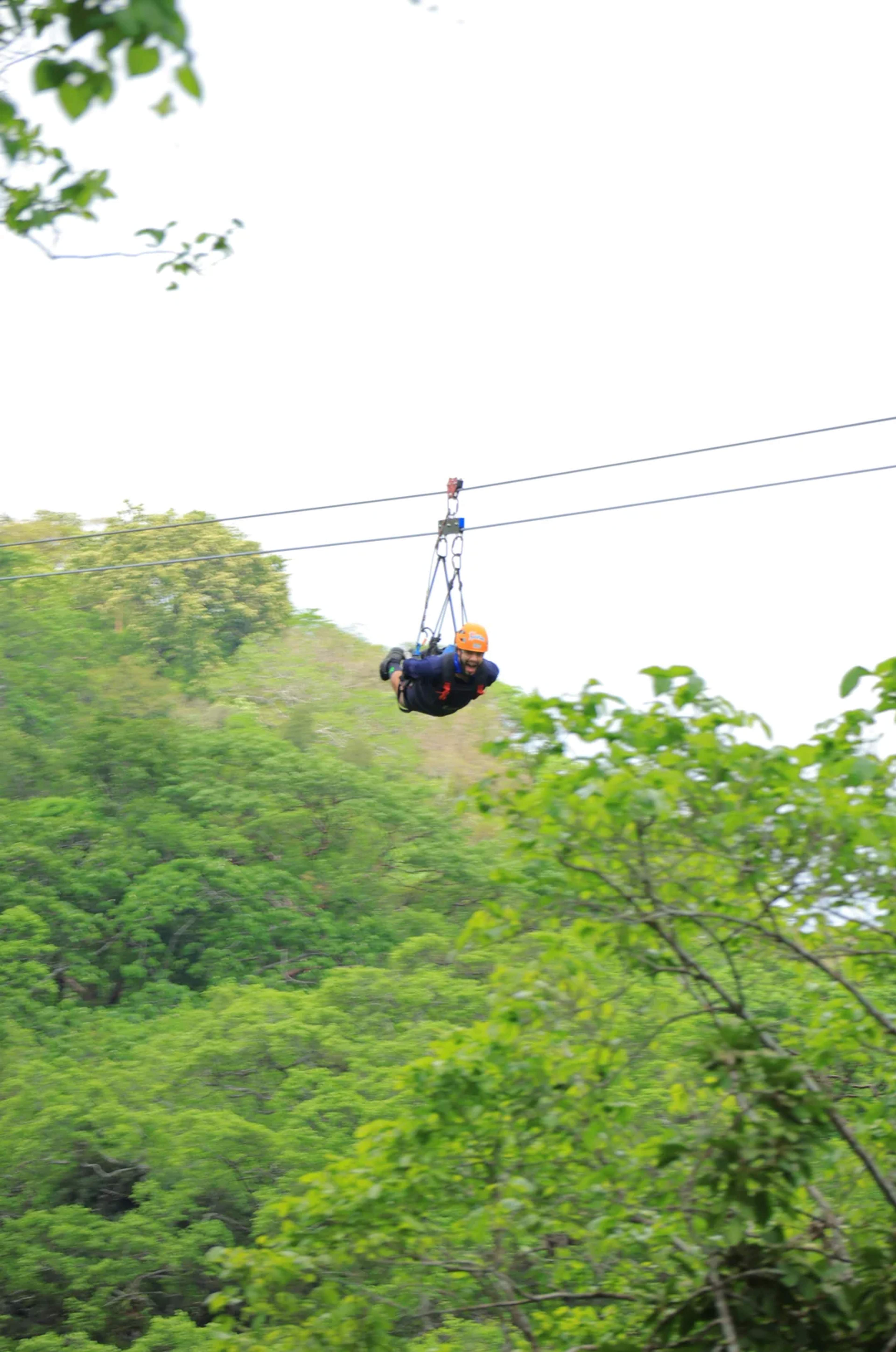 Hombre desliza por la tirolesa entre árboles frondosos, rodeado de naturaleza y adrenalina.