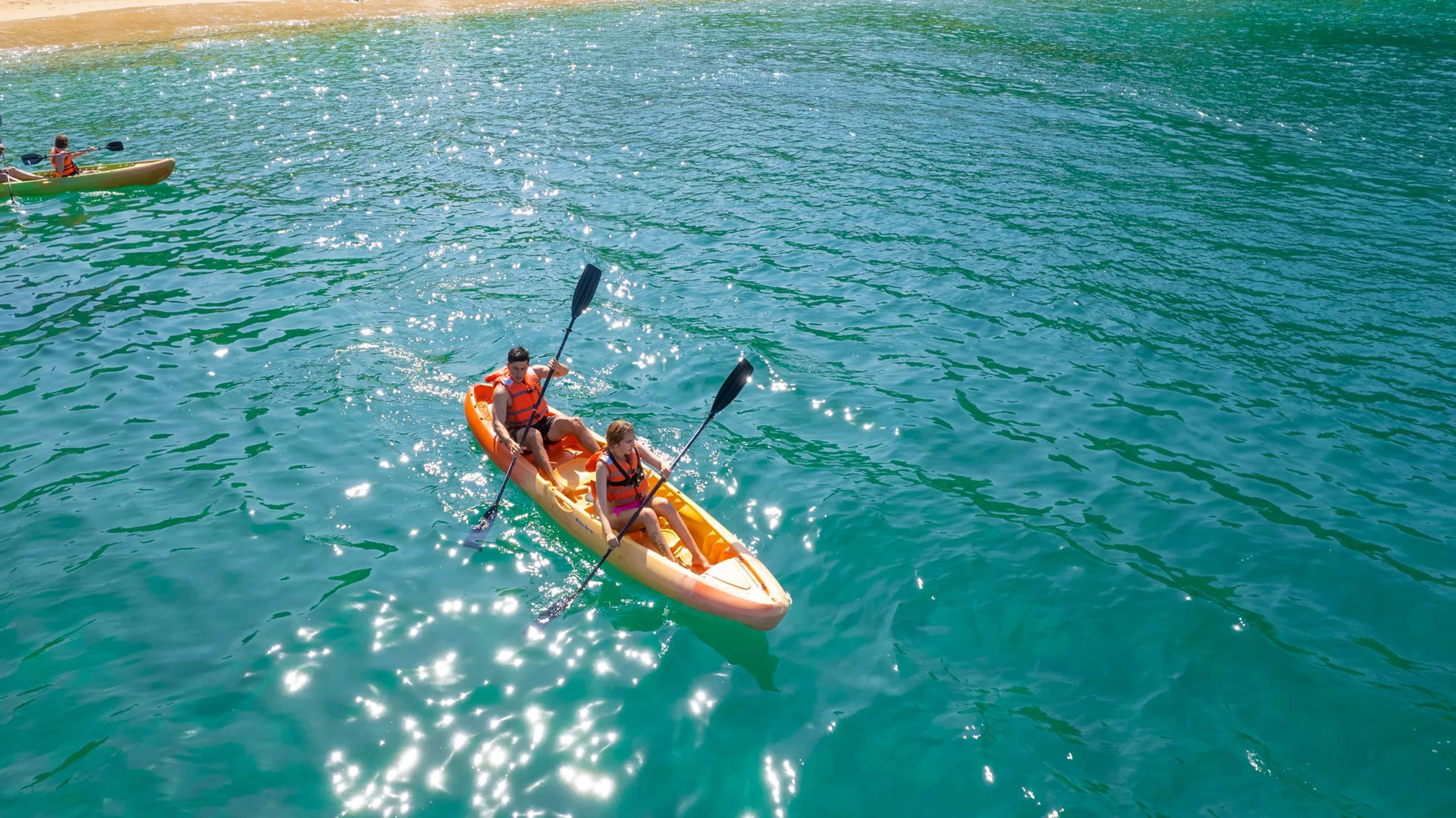 Dos kayakistas reman por las aguas turquesas frente a la playa de Majahuitas, con más kayakistas visibles al fondo.