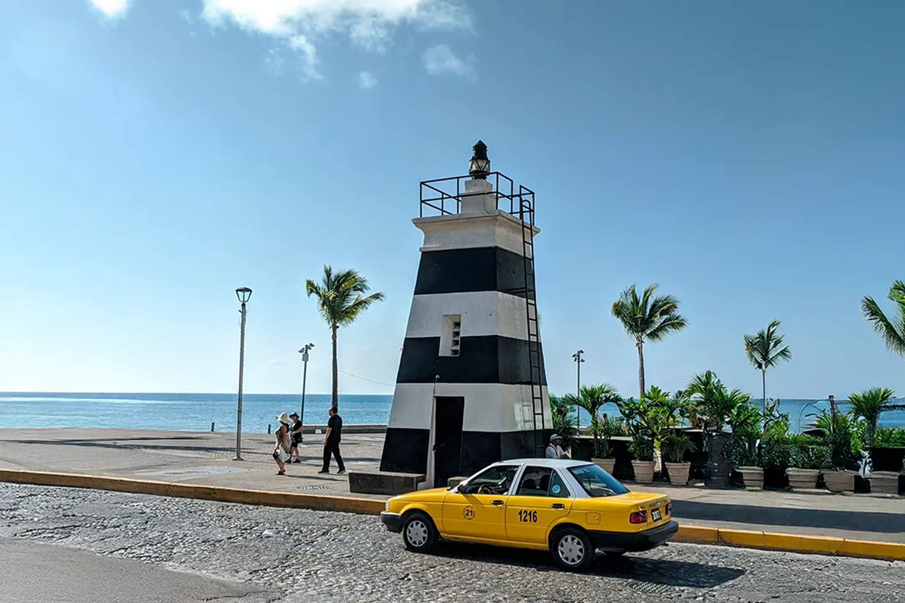Taxi amarillo pasa junto al icónico faro del malecón de Puerto Vallarta.