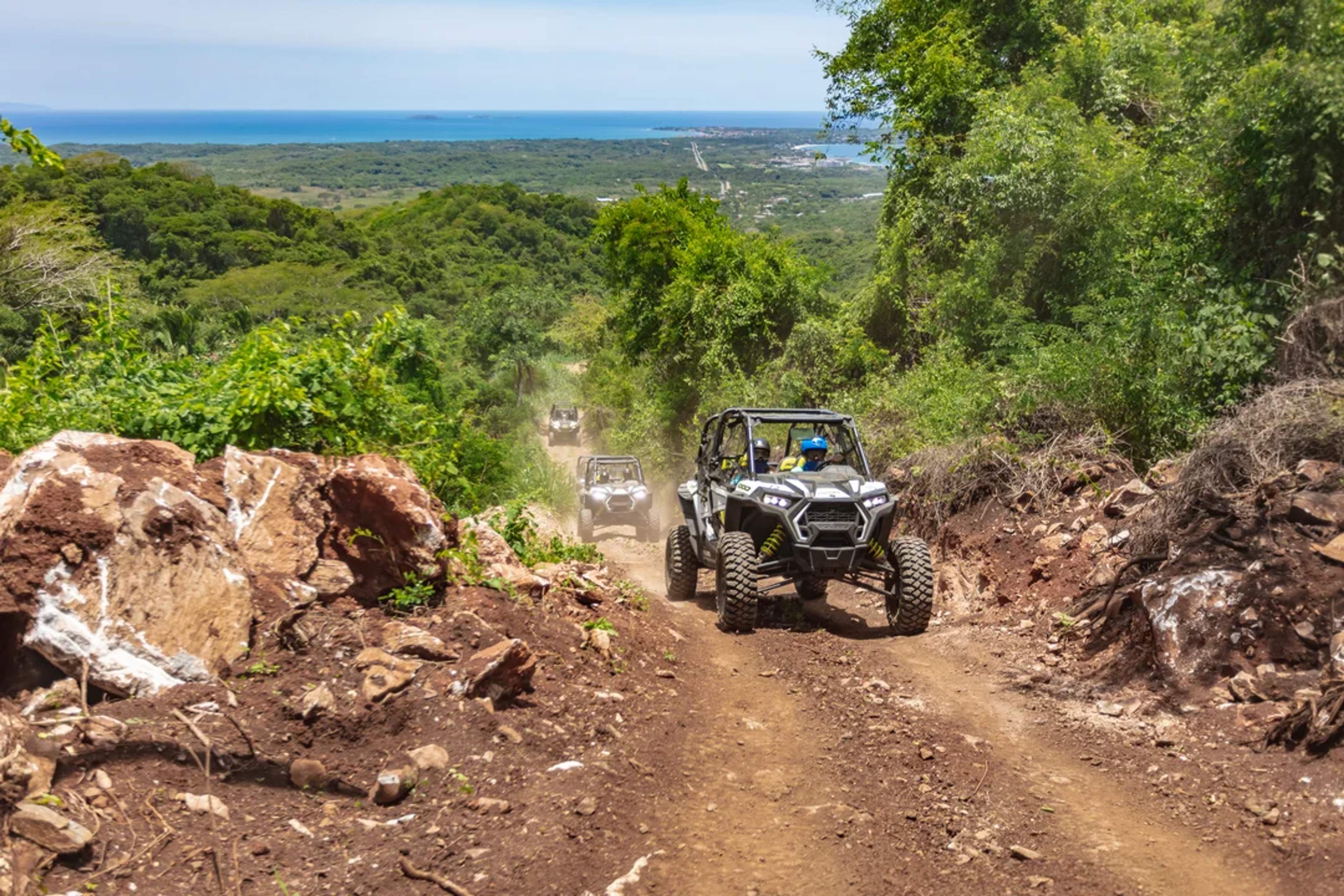 ATVs ride through a jungle trail with ocean views in the distance, adventure in full swing.