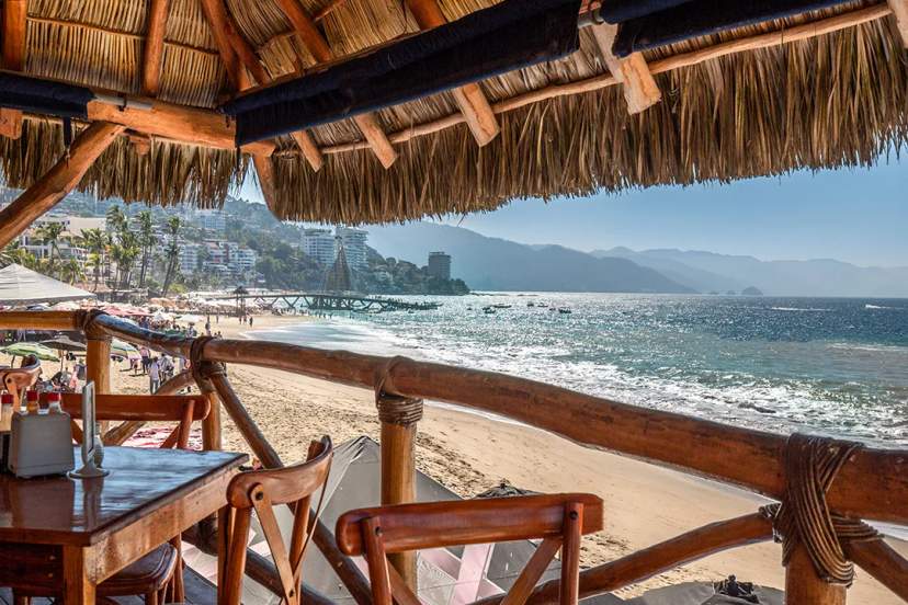 Beachfront restaurant in Puerto Vallarta with ocean views, wooden terrace seating, and the Sierra Madre in the background